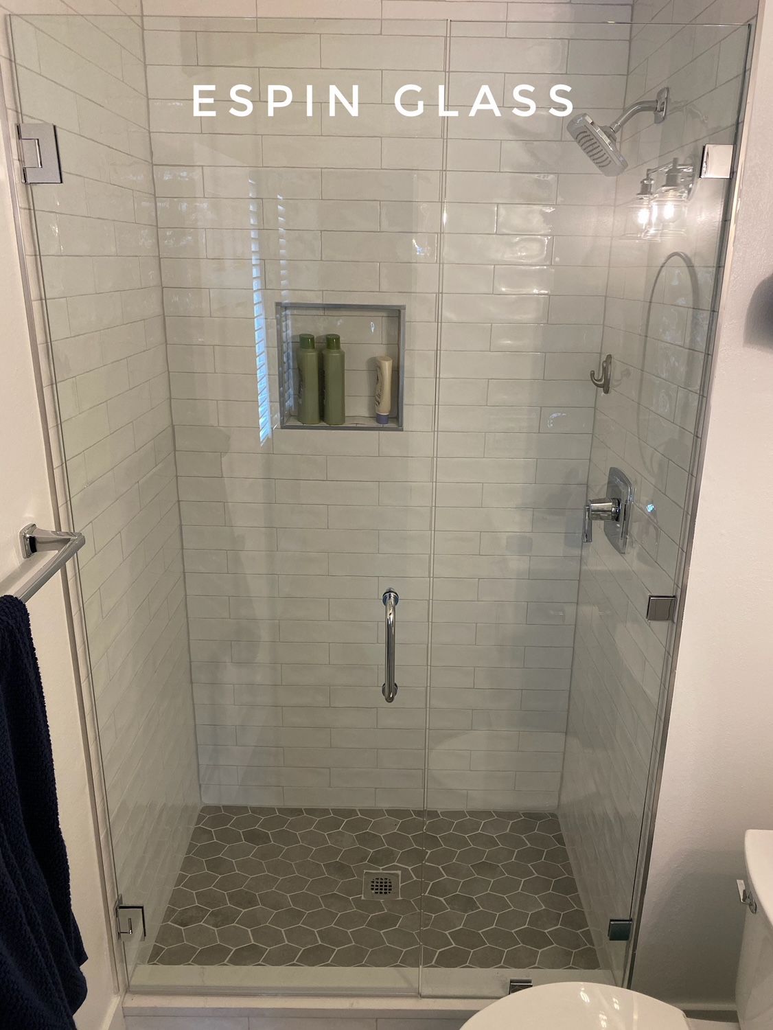 Glass shower enclosure with gray tile floor and white subway tile walls; a built-in shelf holds toiletries.