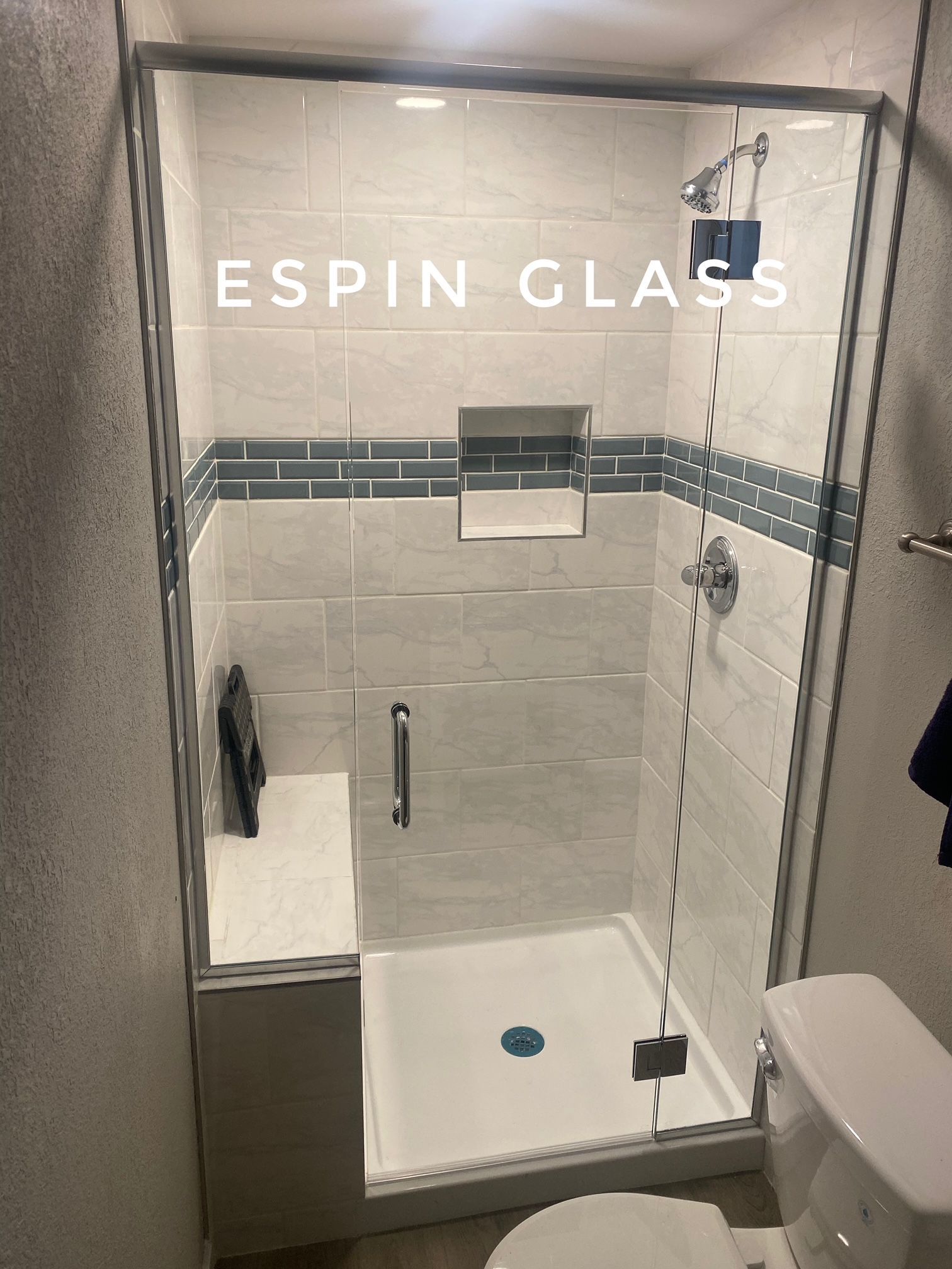 Glass shower enclosure with gray and blue tile, white base and toilet.