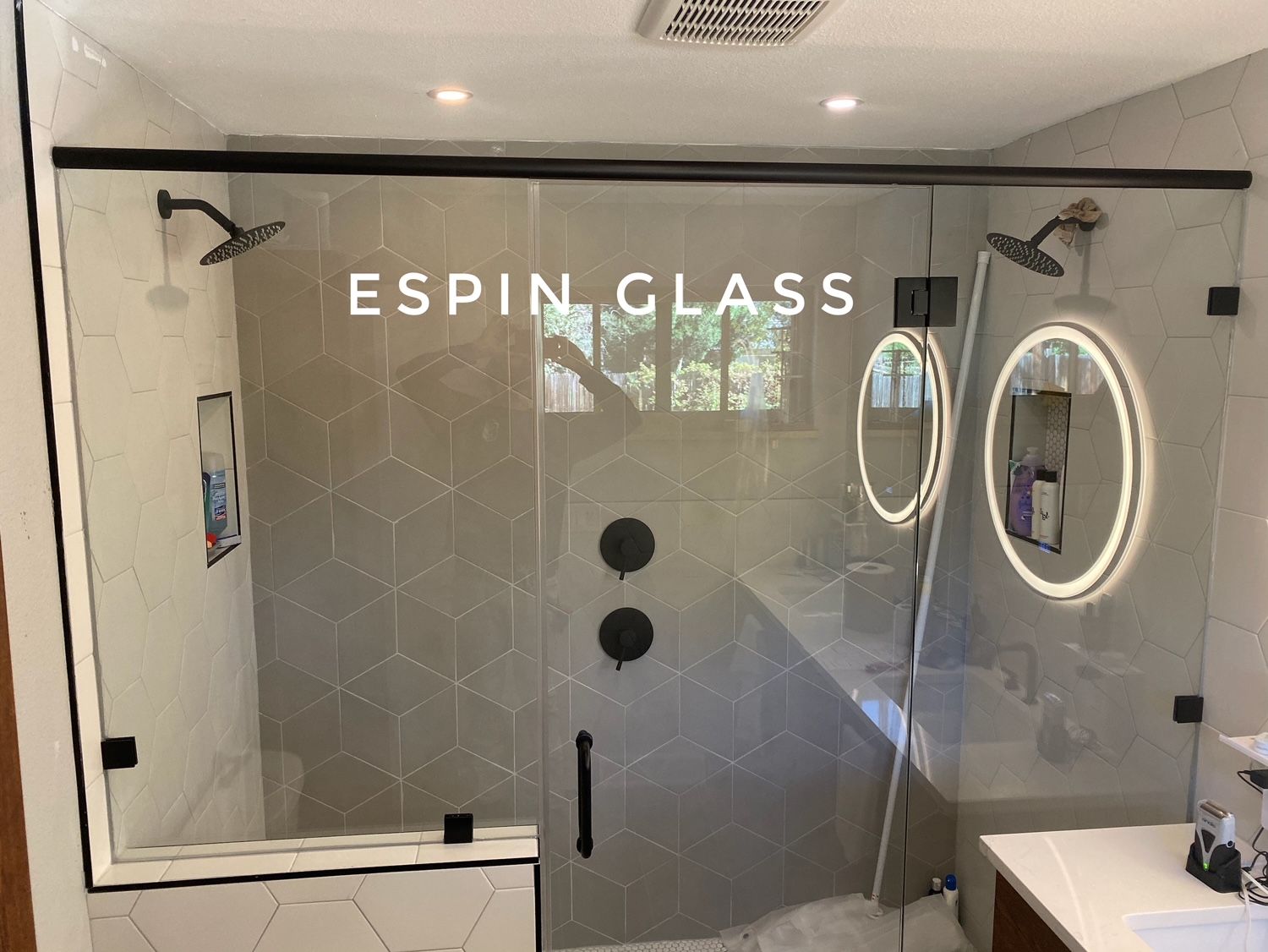 Black framed glass shower with black fixtures and rain shower heads, and a white tiled interior.
