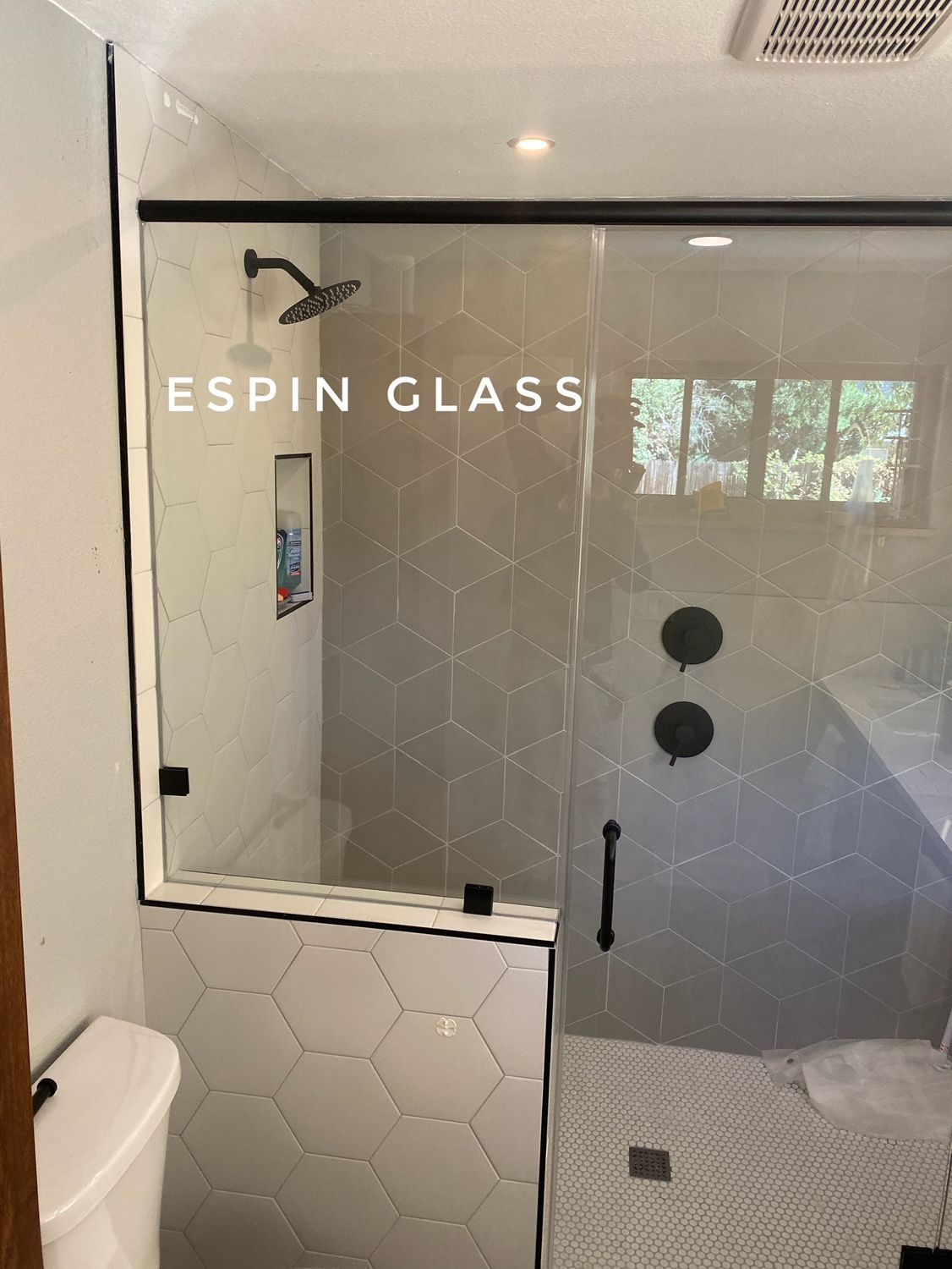 Modern bathroom with glass shower enclosure, black fixtures, hexagon and geometric tiles.