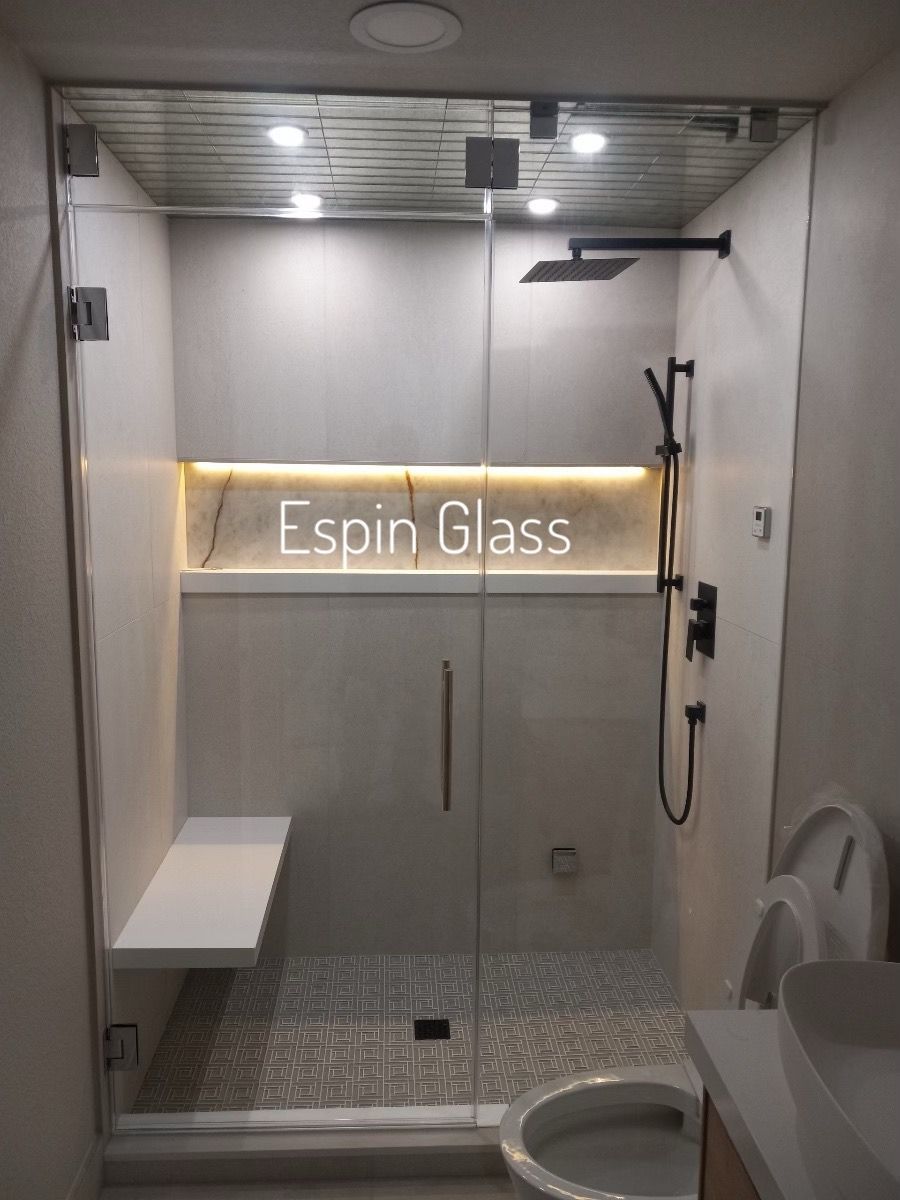 Glass shower with a bench, black fixtures, and inset lighting in a modern bathroom.