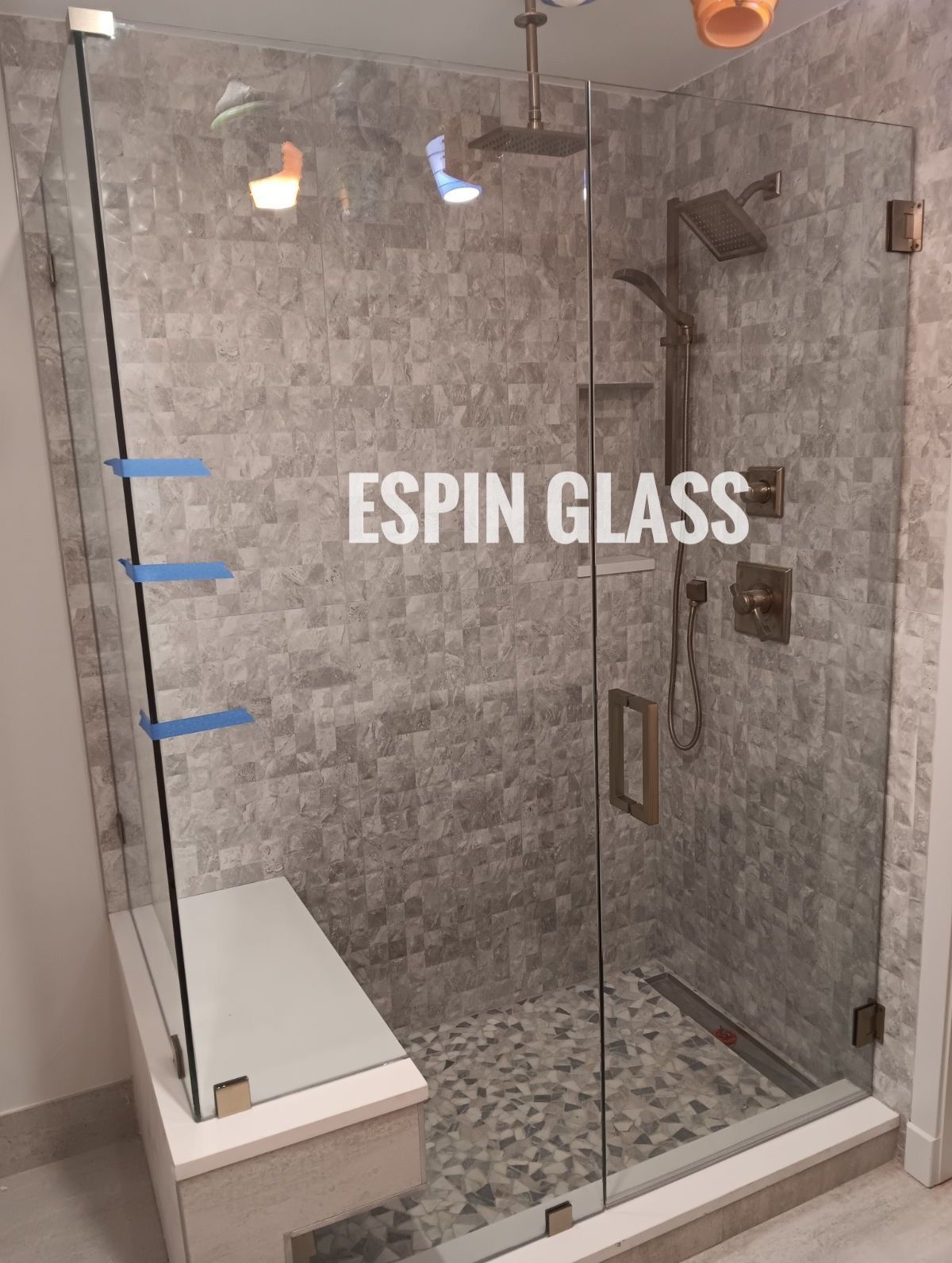 Glass shower enclosure with gray tile, a built-in bench, and chrome shower fixtures.