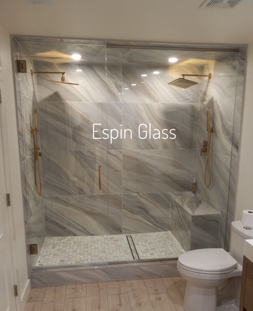 Shower with marble-patterned tile walls, glass doors, gold fixtures, and mosaic tile floor.