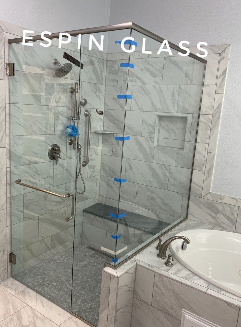 Frameless glass shower enclosure with marble tile walls, a seat, and a bathtub.