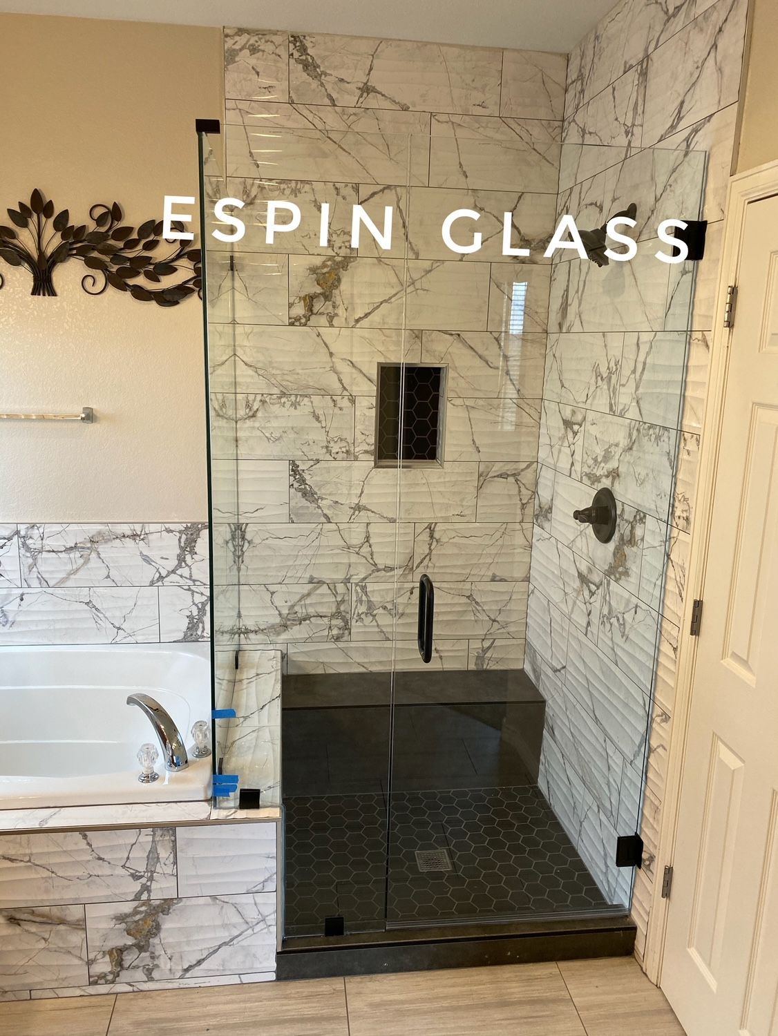A modern bathroom with a glass shower enclosure, marble tiles, and black accents.