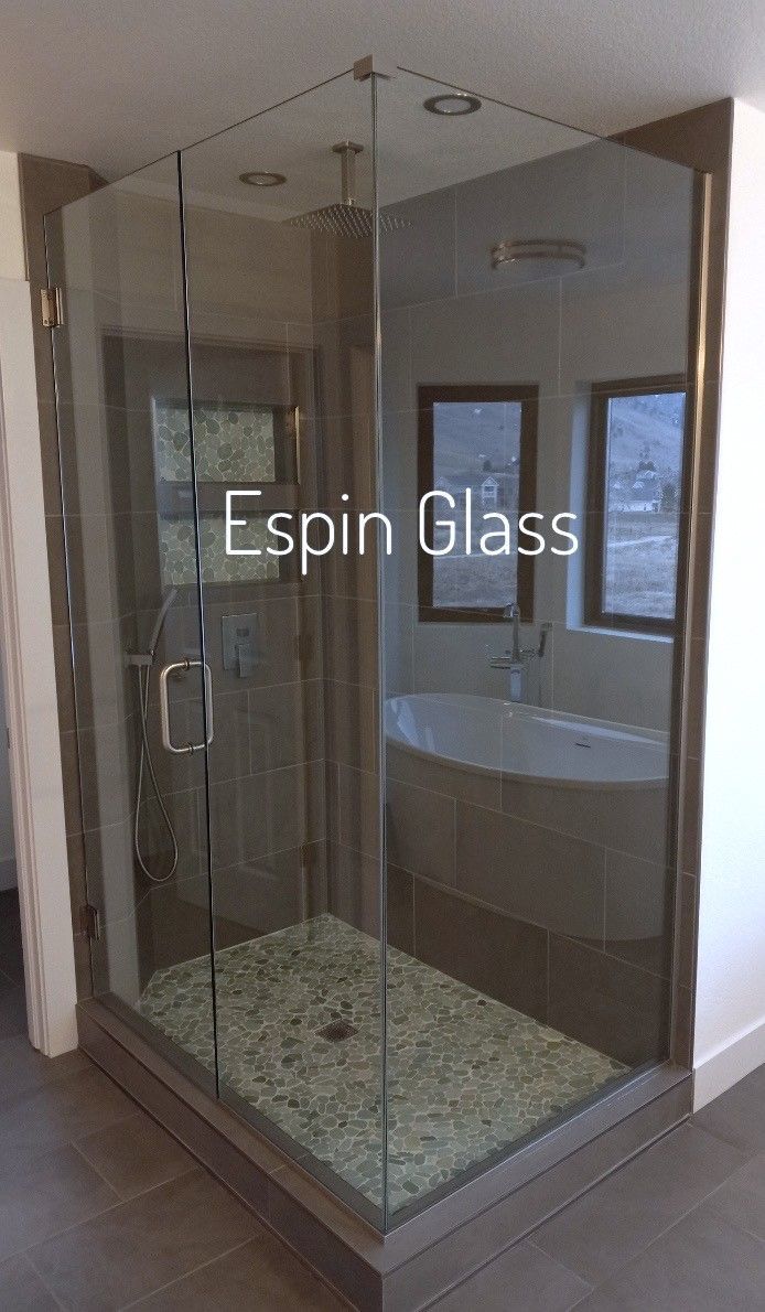 Frameless glass shower with pebble floor, next to a bathtub in a bathroom.