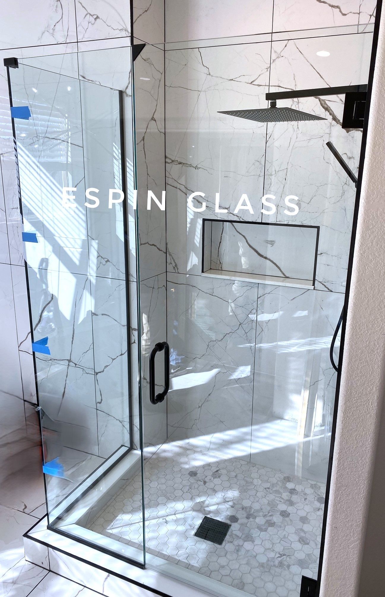 Glass shower enclosure with black fixtures and marble tile.