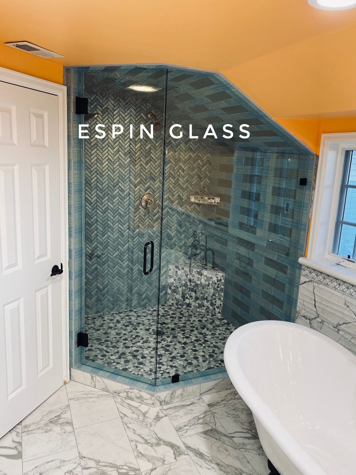 A modern bathroom with a glass shower enclosure, white tub, and marble tile, illuminated by natural light.