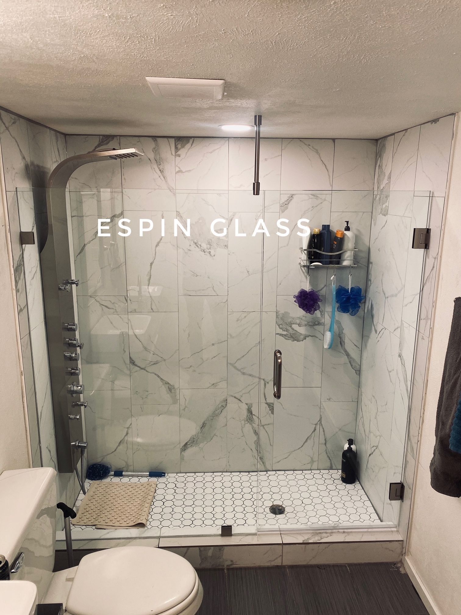 Bathroom with marble-look tile shower. Glass door and wall, chrome fixtures. Toilet in foreground.