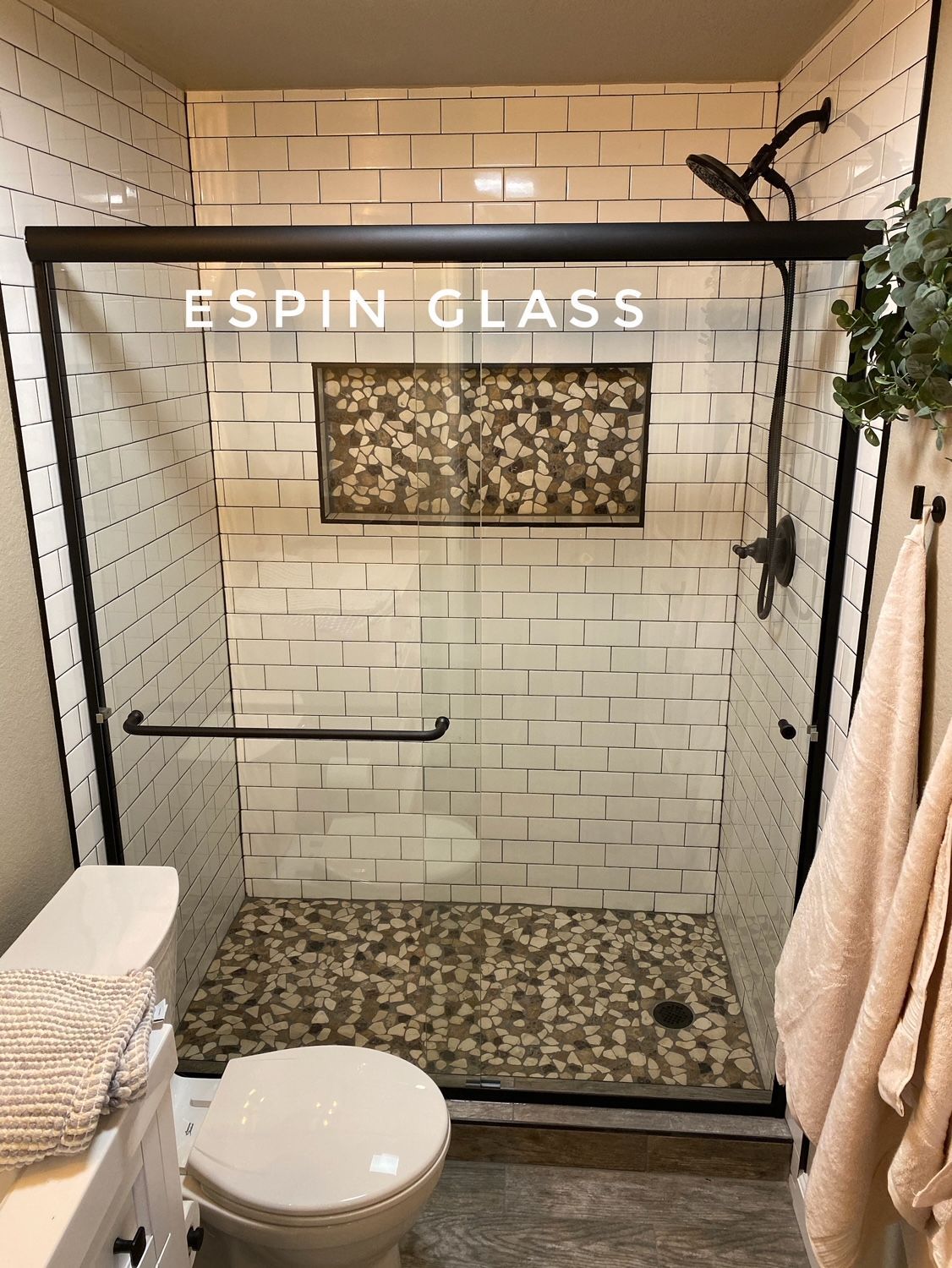 Black-framed glass shower in a bathroom with white subway tile walls and a mosaic tile floor.