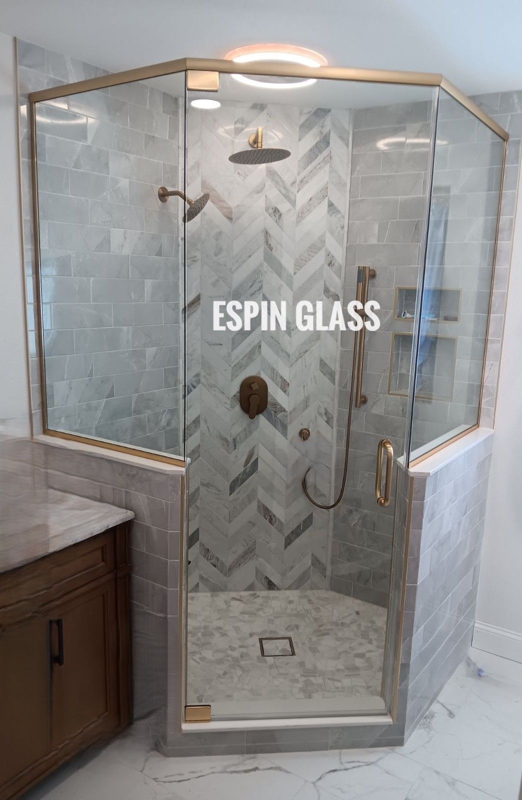 Angled glass shower enclosure with gold hardware, gray tile, and marble accents.