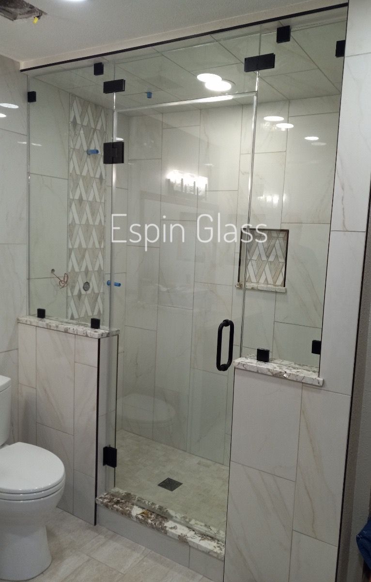 Glass shower enclosure in a tiled bathroom with black hardware and a toilet.