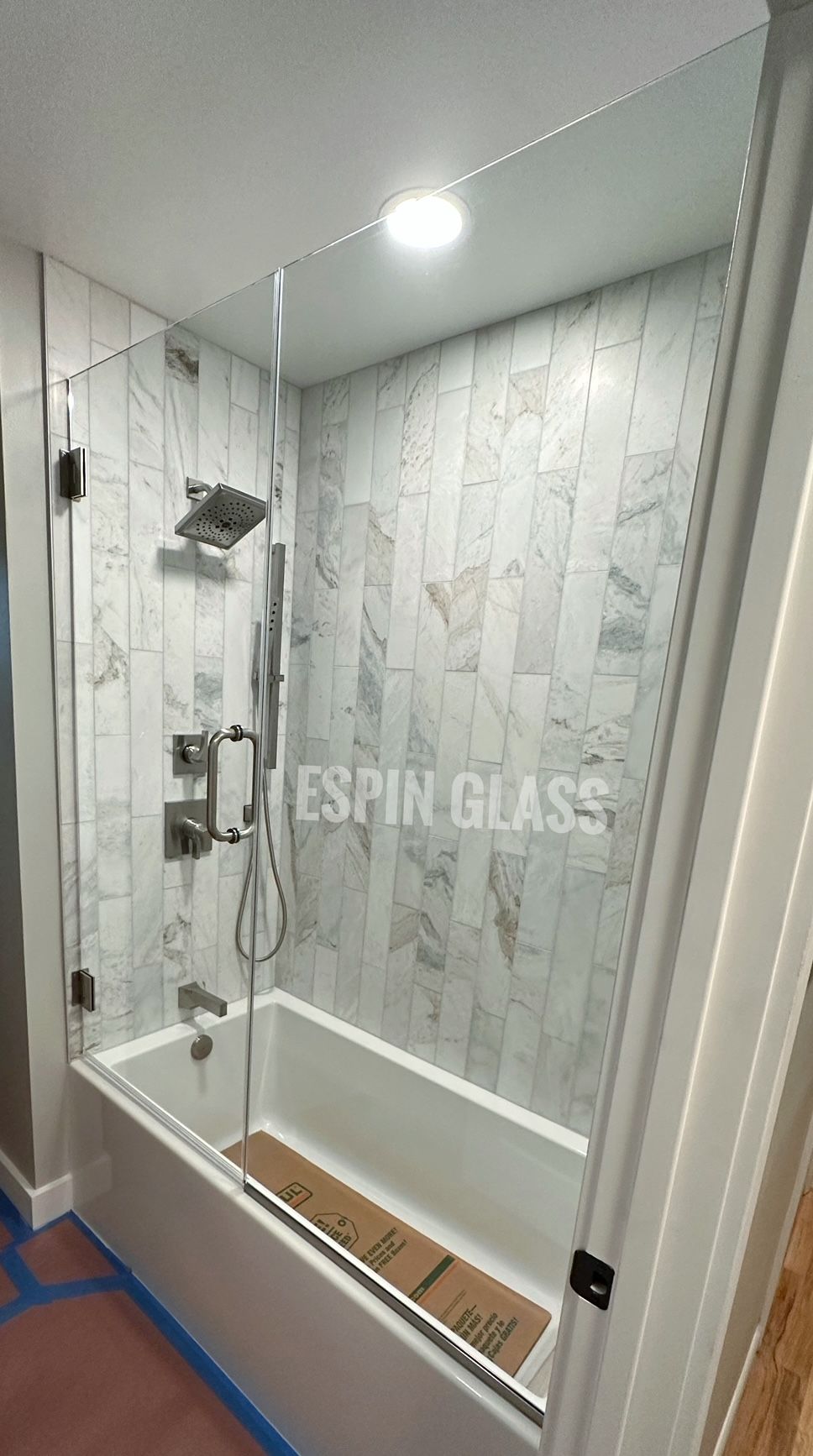 Shower with clear glass enclosure and white marble tile, silver fixtures, and a white tub.