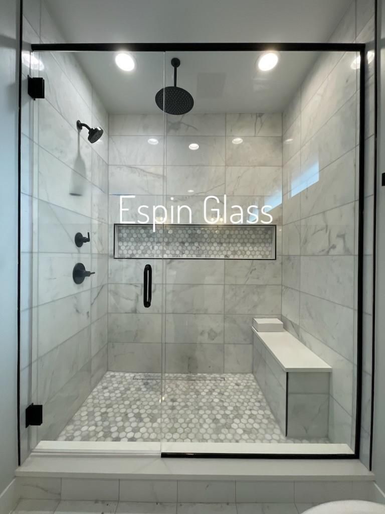 Modern shower enclosure with black trim, glass door, and marble tile.