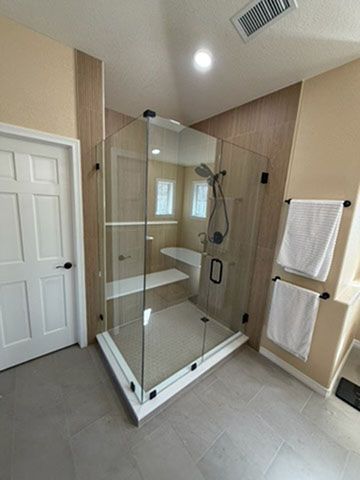 Modern bathroom with a glass walk-in shower, beige tile walls, and white towel racks.
