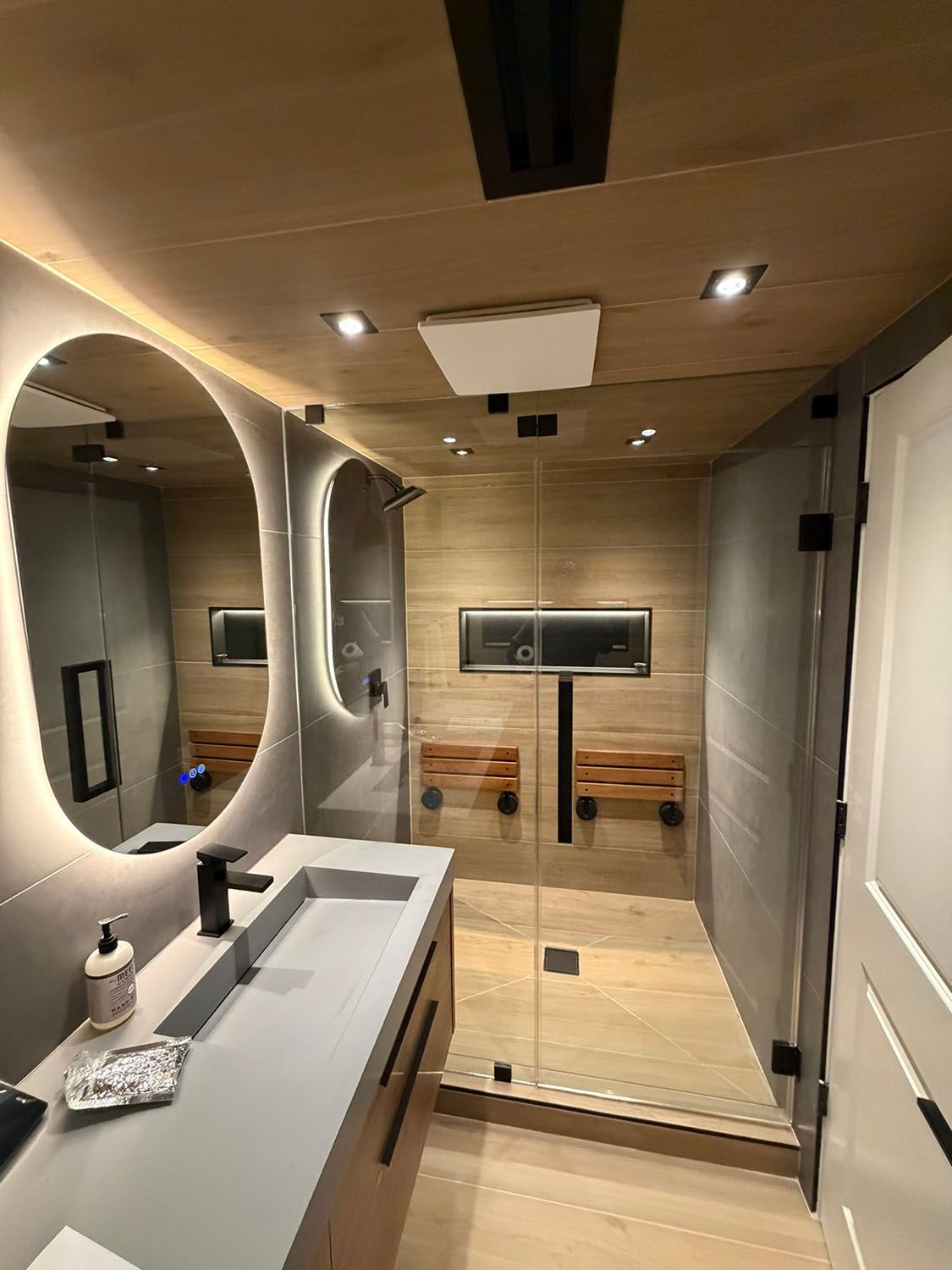 Modern bathroom with sink, mirror, wood-paneled walls, and glass shower enclosure.