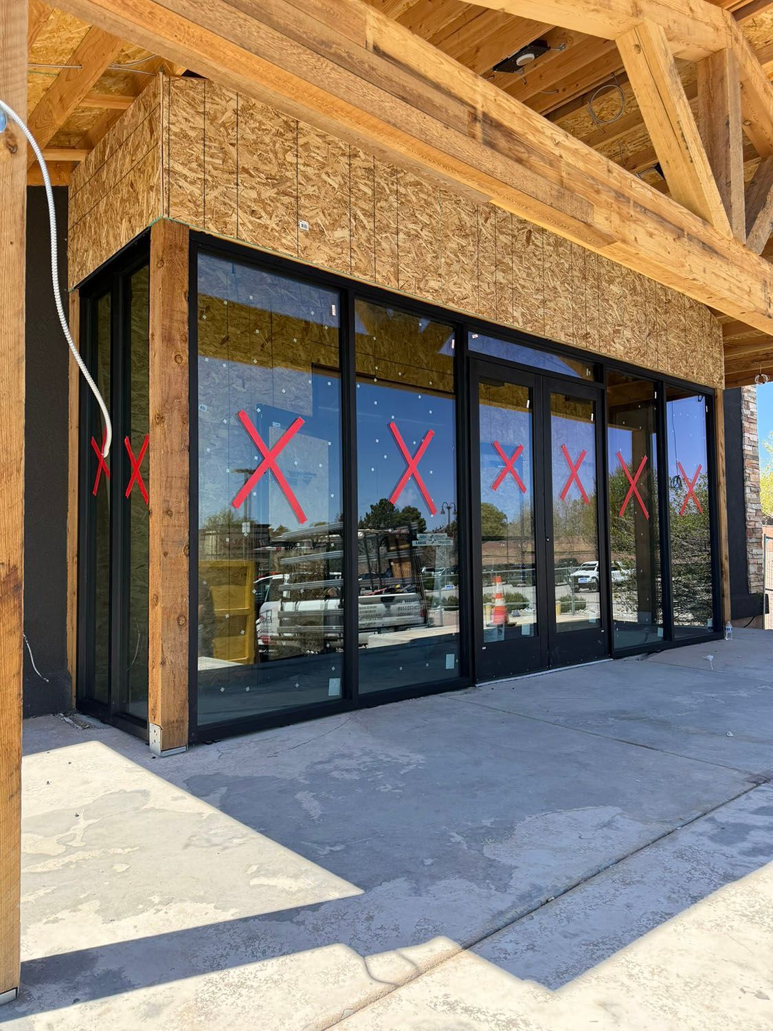 Glass storefront with red X marks on windows under construction at a wooden building.