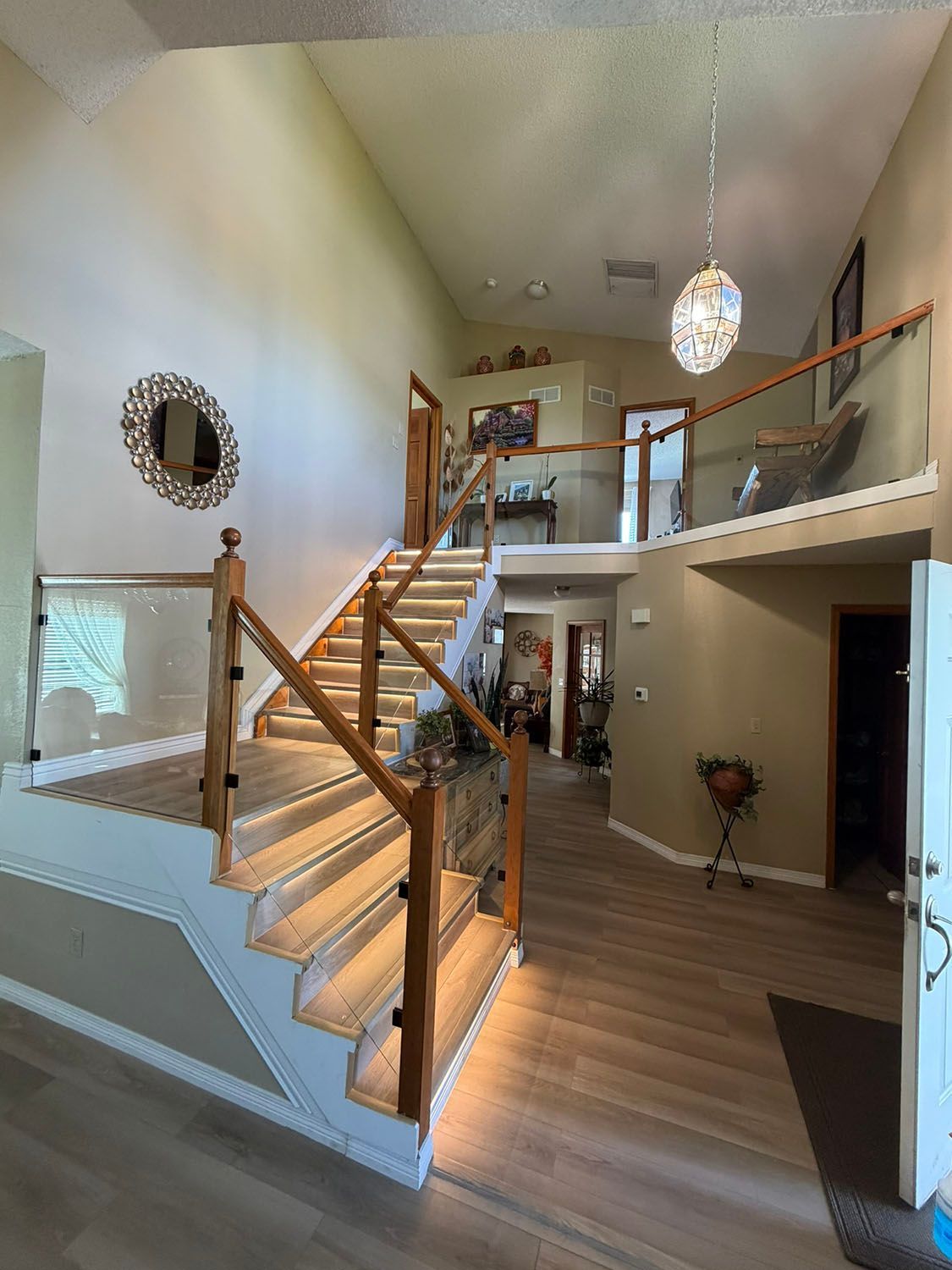 Bright two-story foyer with wood staircase, balcony railing, hanging pendant light, and hardwood floors.