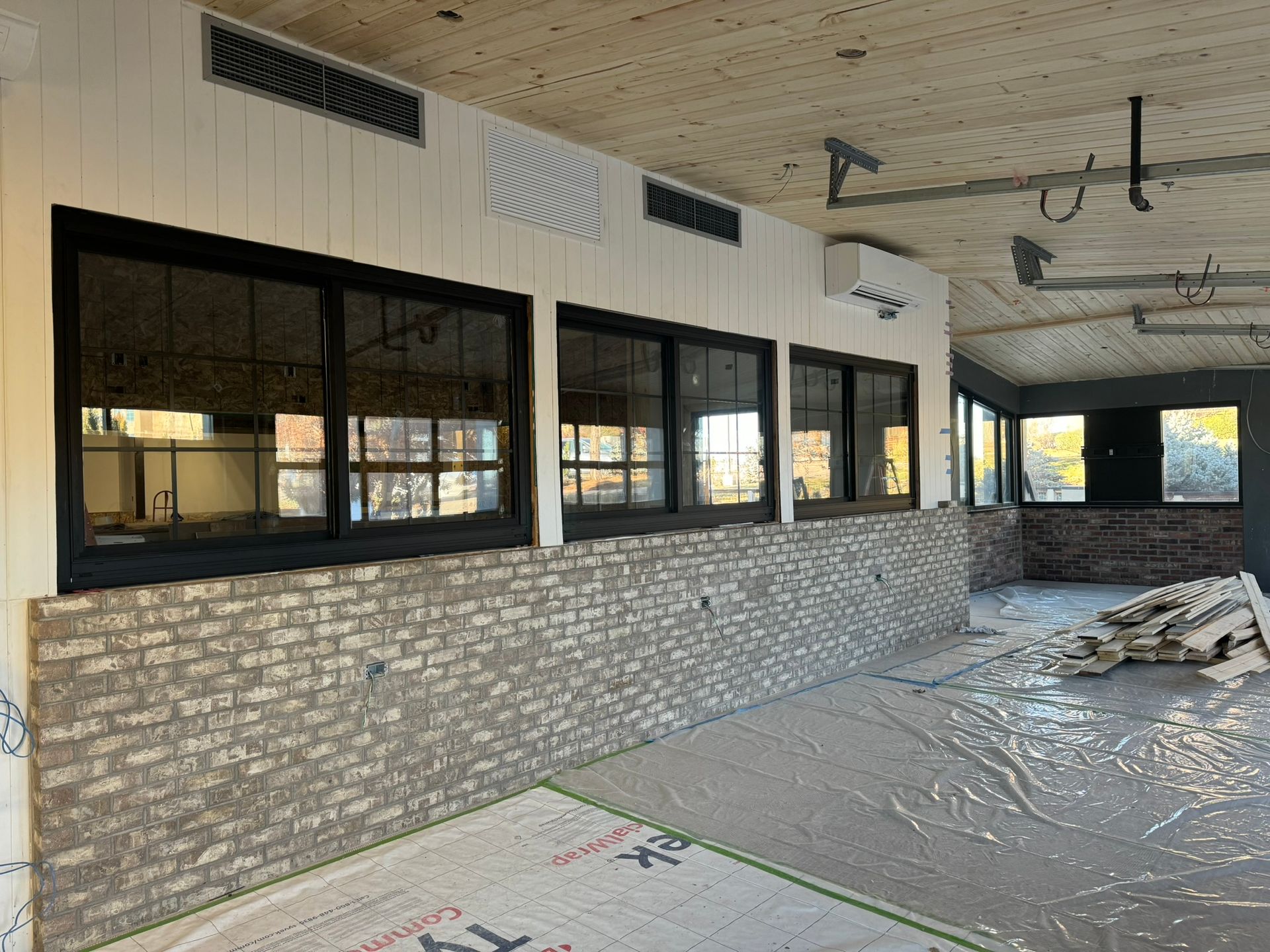 Abandoned room with exposed brick, black windows, and debris on the floor during renovation.
