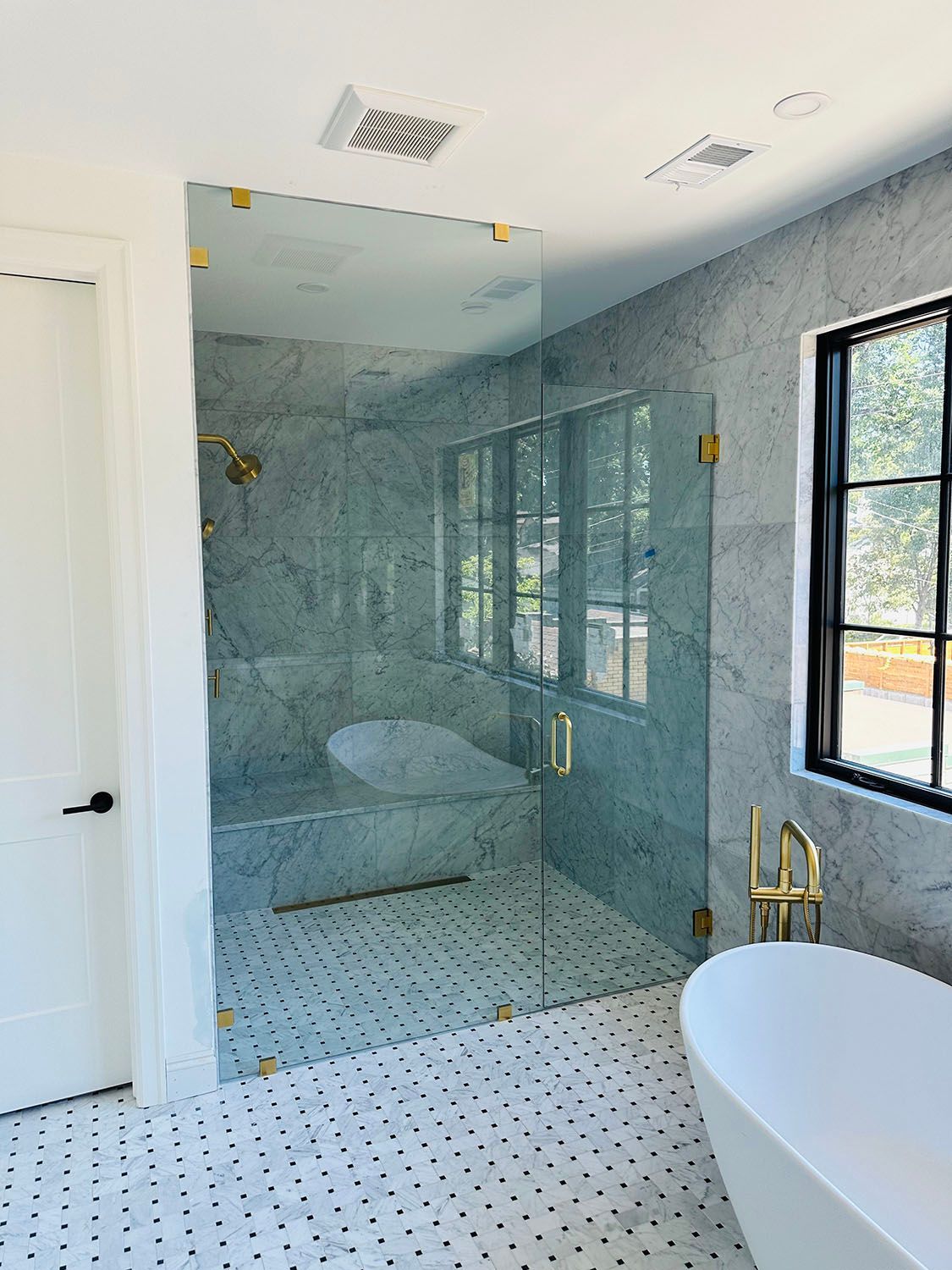 Modern bathroom with glass walk-in shower, marble tile, and freestanding tub.