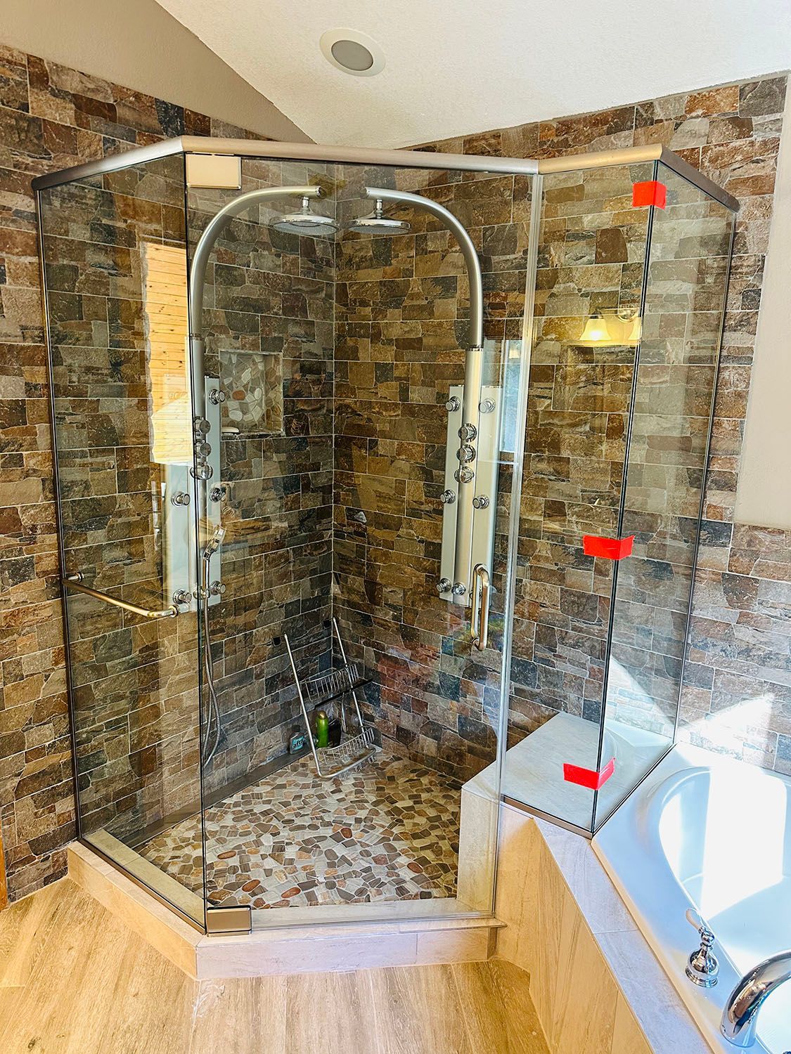 Curved glass walk-in shower with stone-tile walls, mosaic floor, and chrome fixtures.
