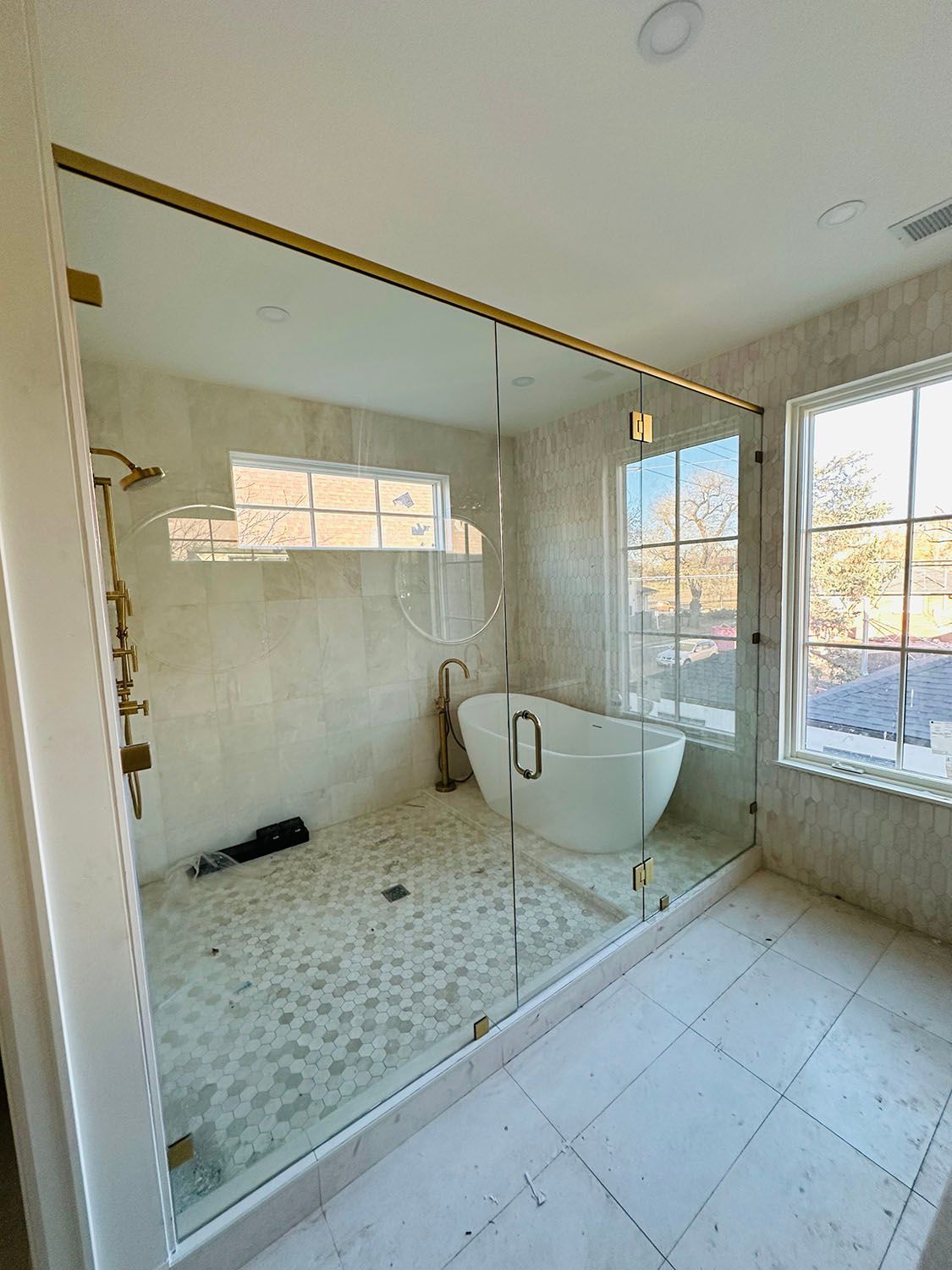 Bright bathroom with glass shower enclosure, freestanding tub, and large windows overlooking trees.