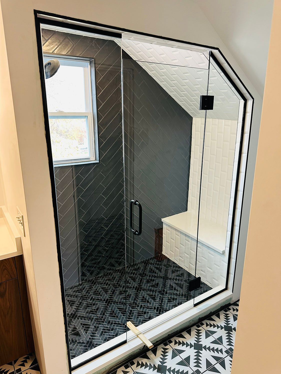 Walk-in shower with black tile and a glass door in a bathroom corner.