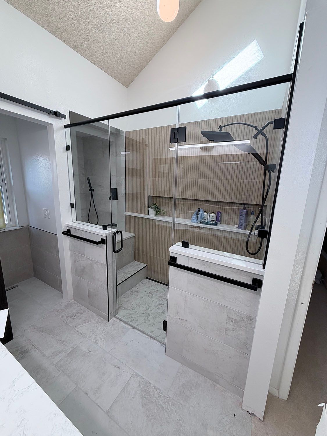 Modern bathroom shower with black-framed glass doors, white tile, and vanity sink.