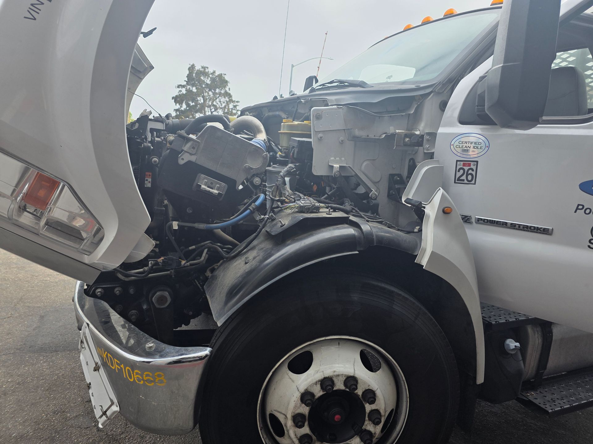 Damaged white semi-truck after front-end collision on a wet road, hood and bumper crushed