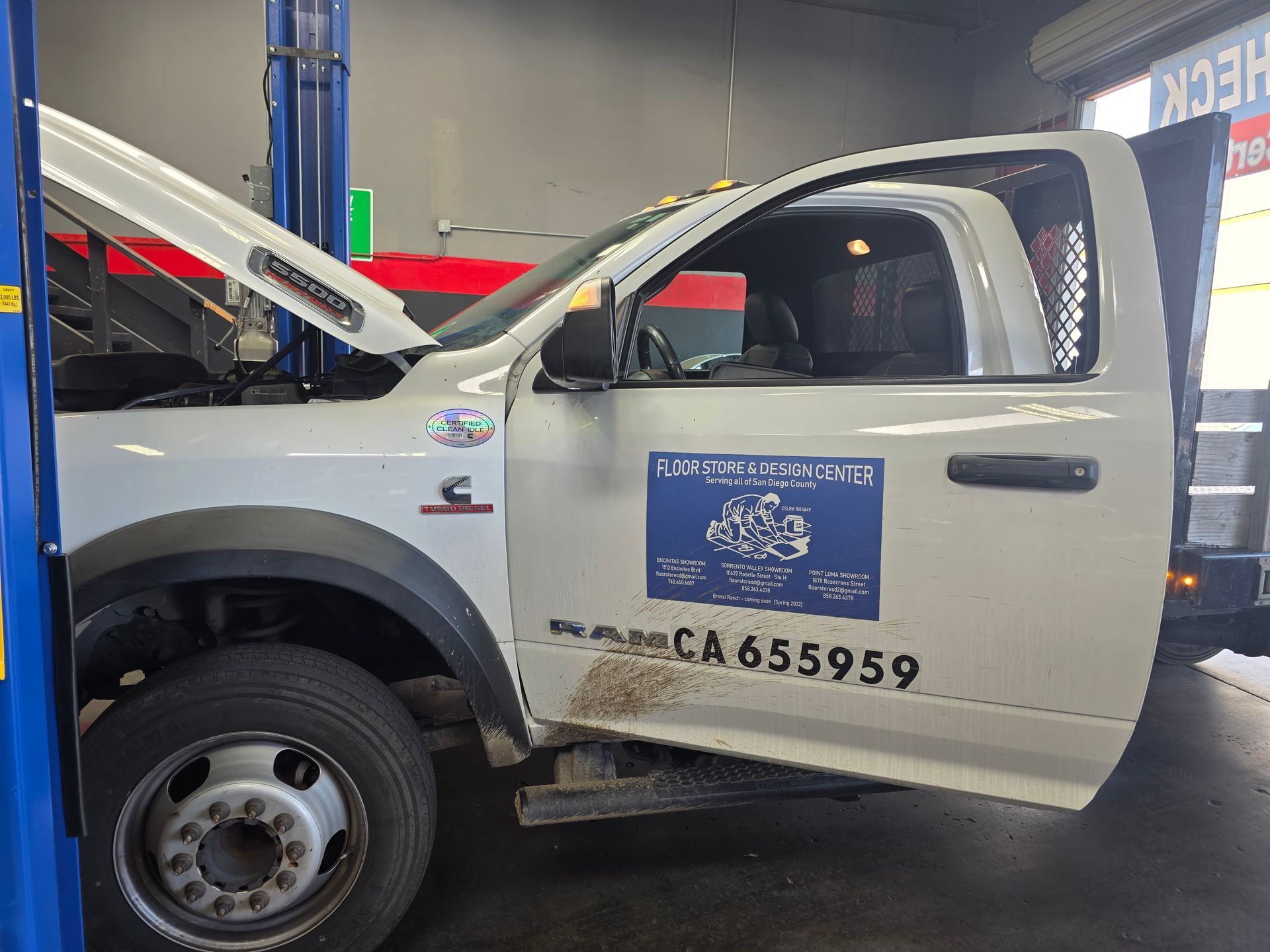 White pickup truck with open hood and driver door in an auto shop garage, side decal visible
