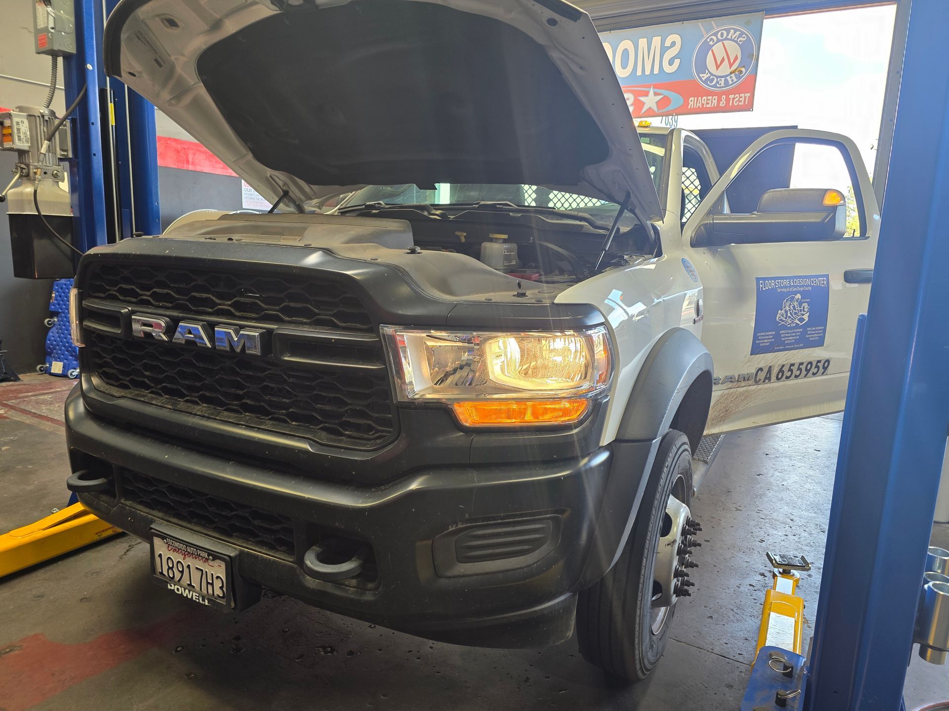 Gray RAM truck in an auto shop with hood open and driver door ajar on a lift.