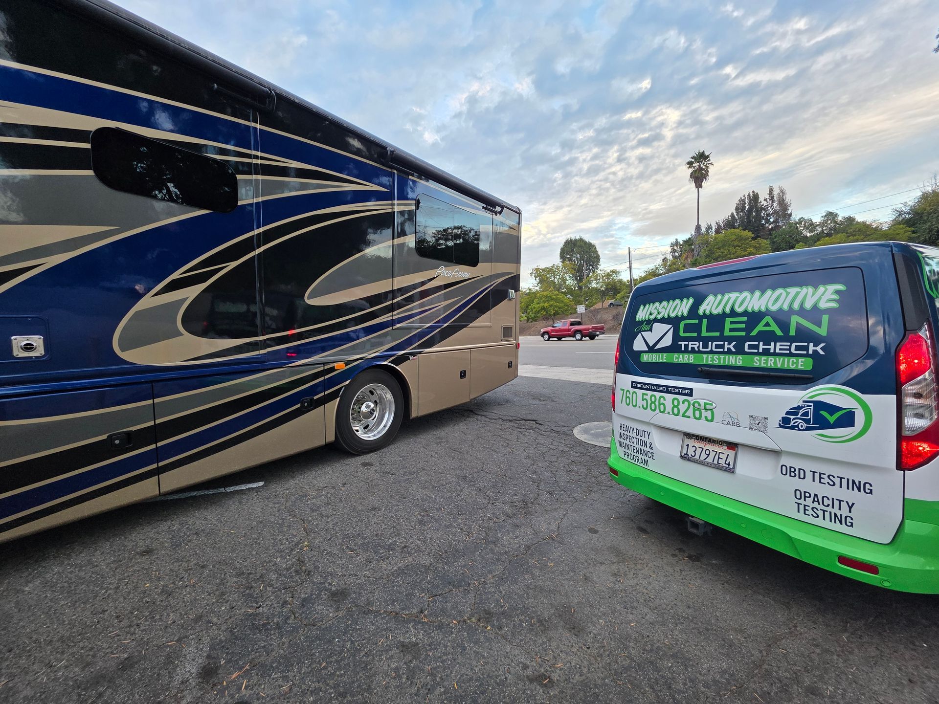 Parked tour bus beside a green-and-white automotive service van in a lot at dusk