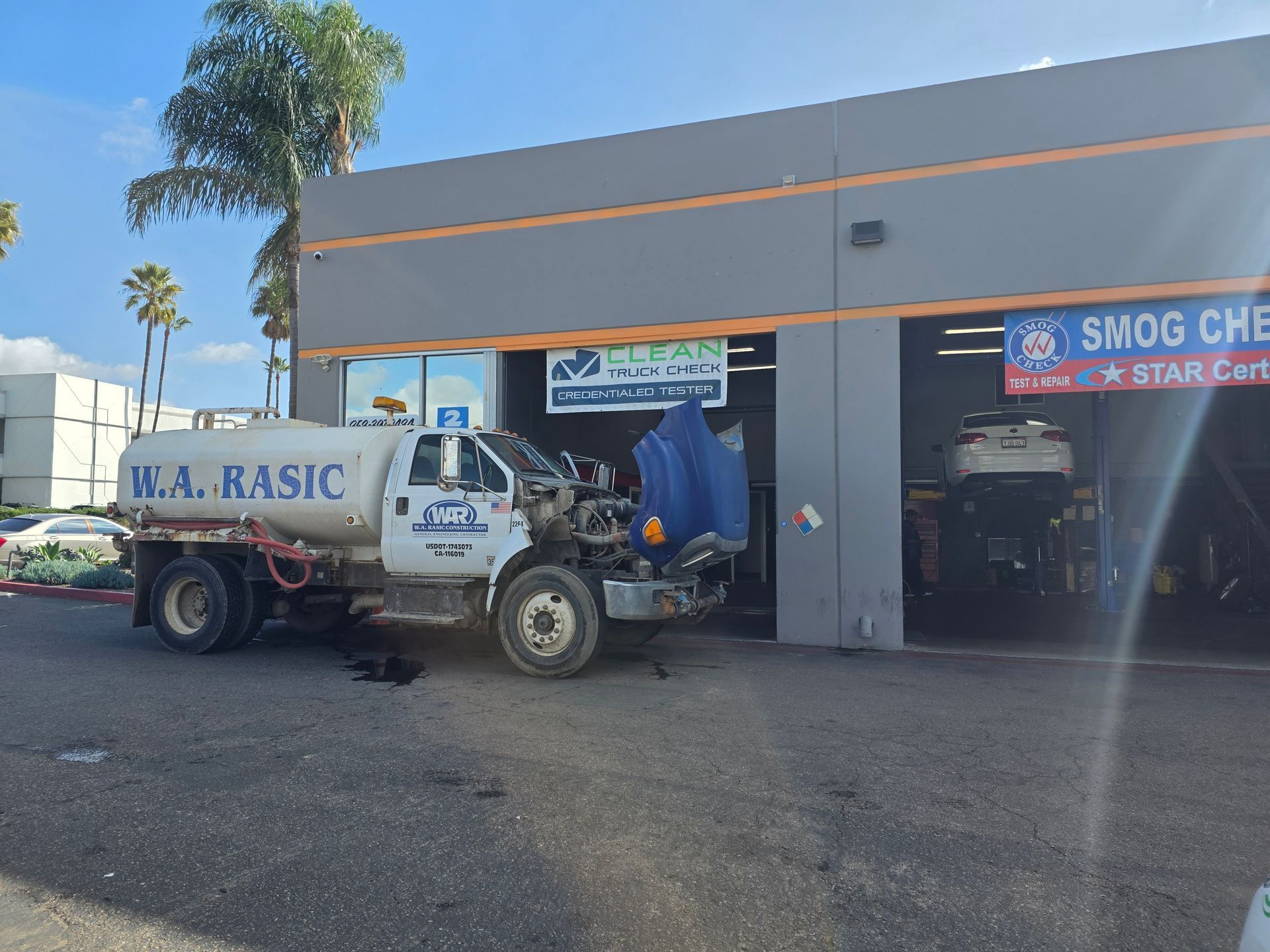 White water truck parked outside a gray building with an orange stripe and shop signs.