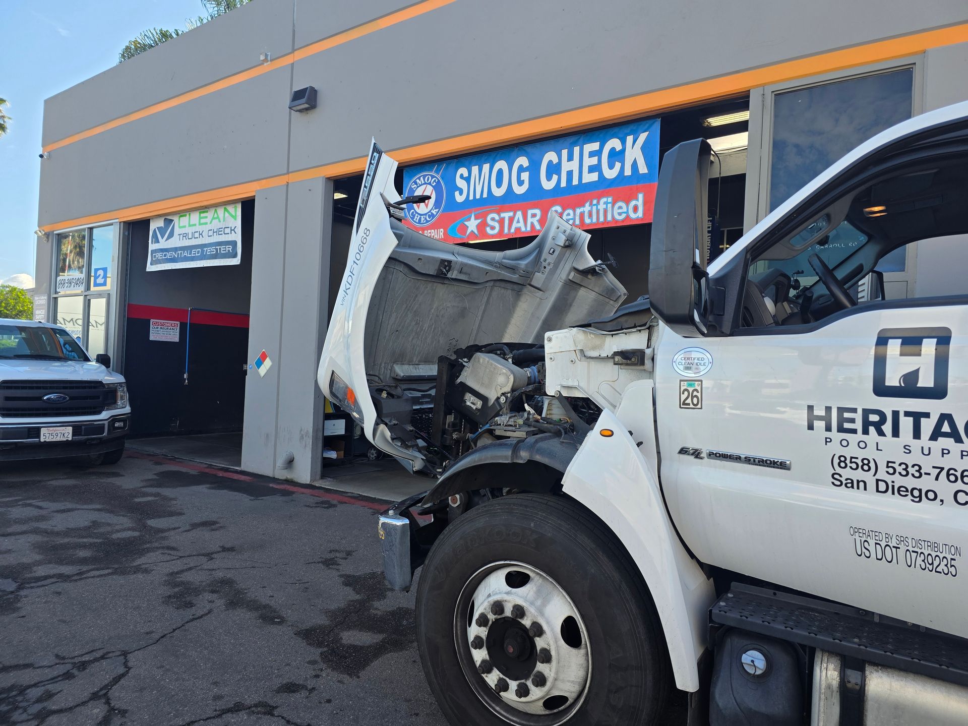 Damaged white truck crashed into a storefront beneath a “SMOG CHECK” sign