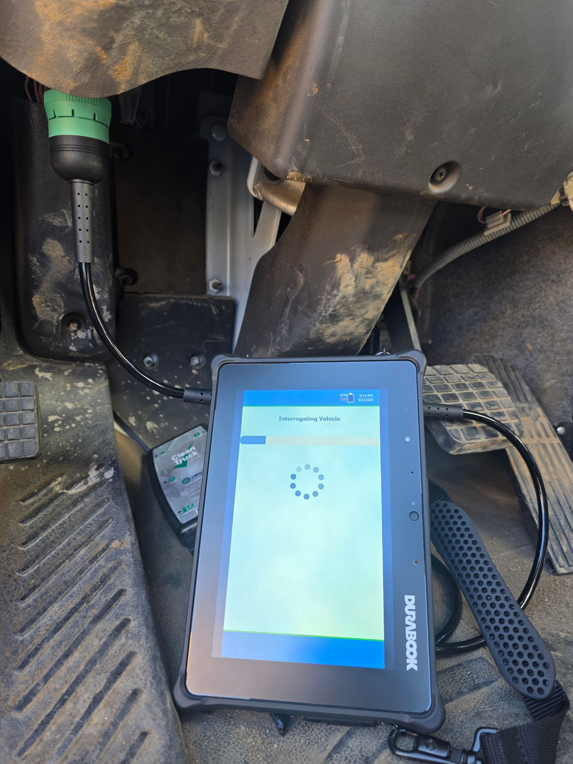 Diagnostic tablet connected under vehicle dashboard, showing loading screen on blue display.