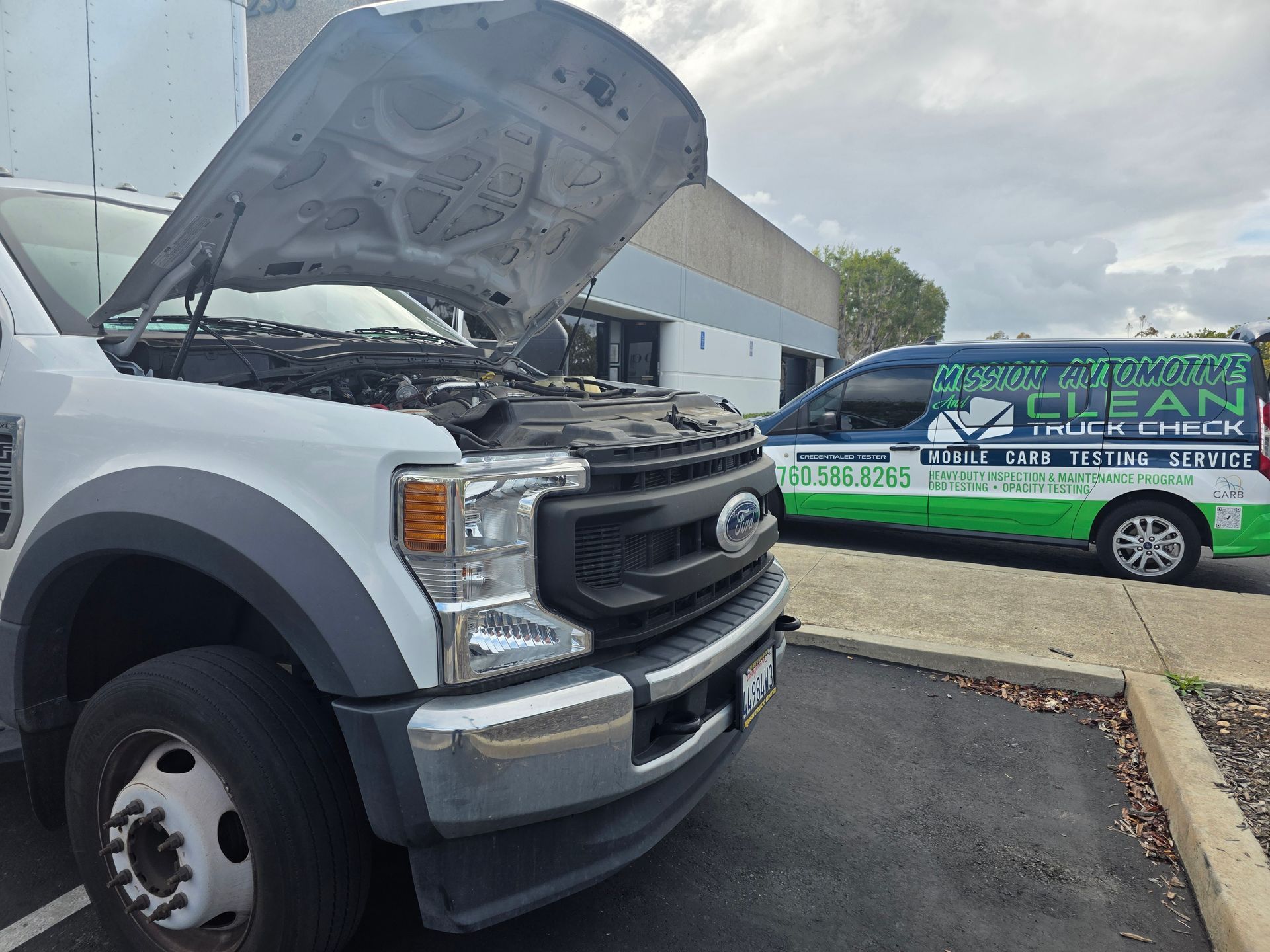 Silver Ford truck with hood open in a parking lot, with a green-and-white van parked nearby.