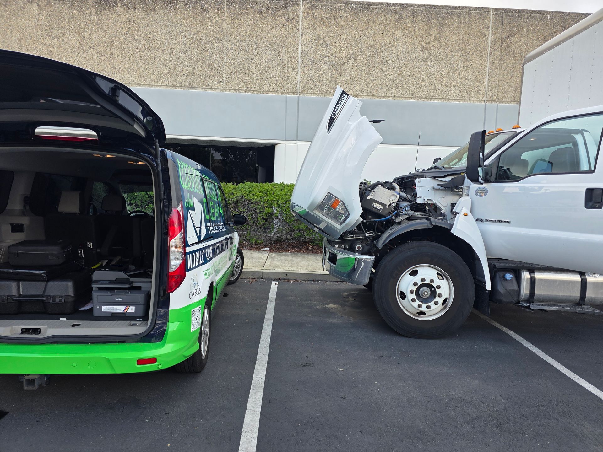 Green van with open rear hatch facing a damaged silver truck in a parking lot.