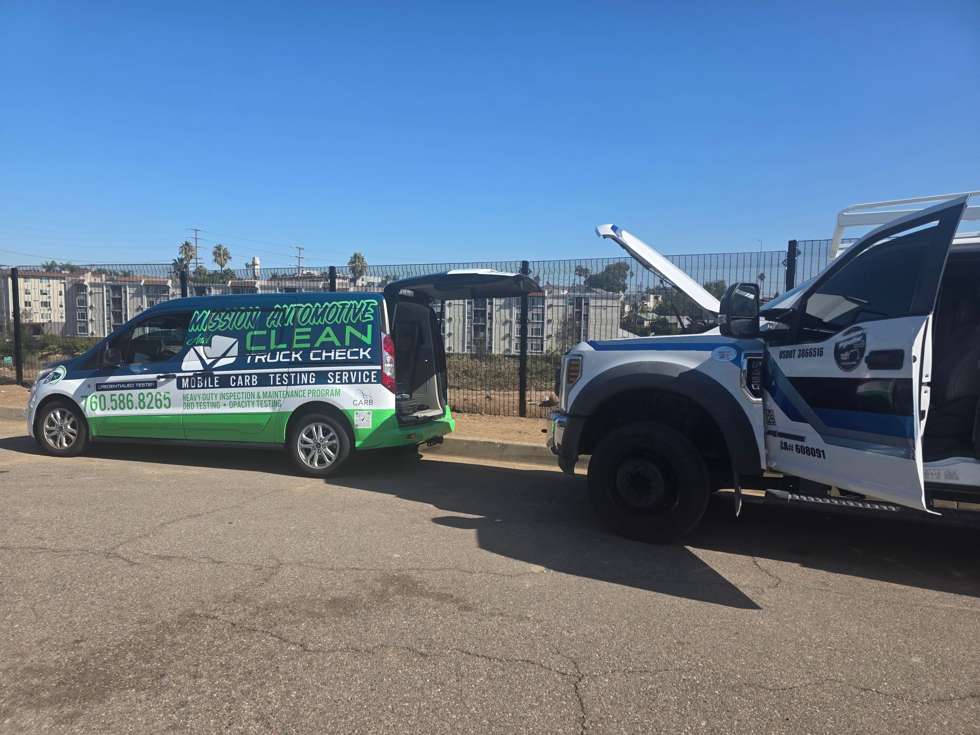 Green and white van towing a blue pickup truck in a parking lot under a clear sky