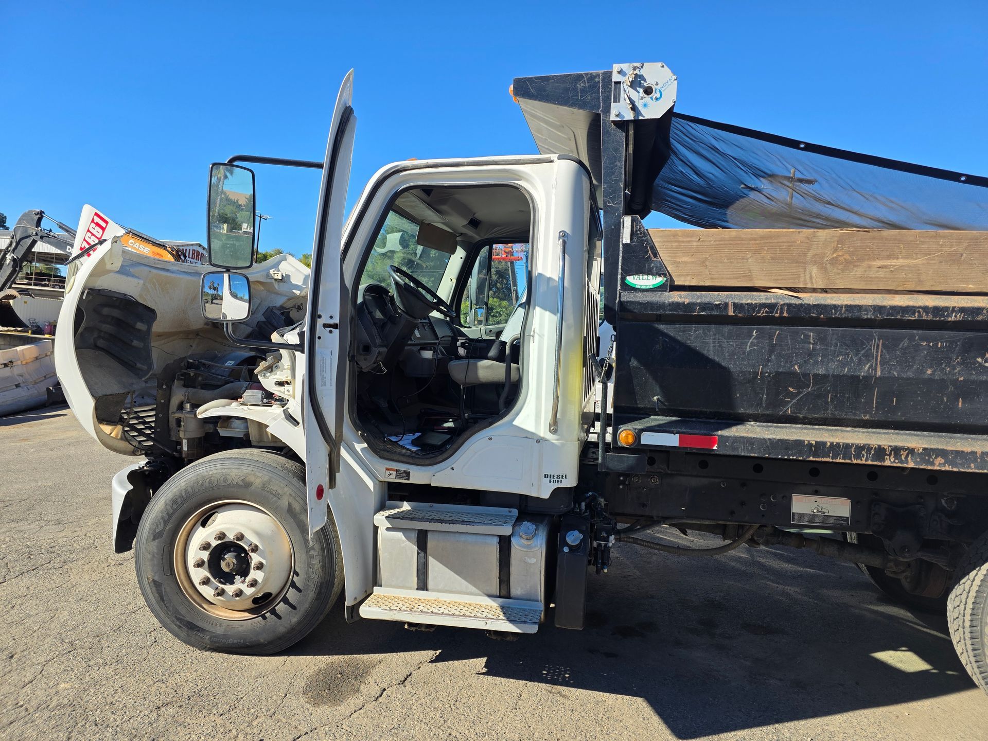 White dump truck parked in a lot, side view with raised front attachment and black cargo bed