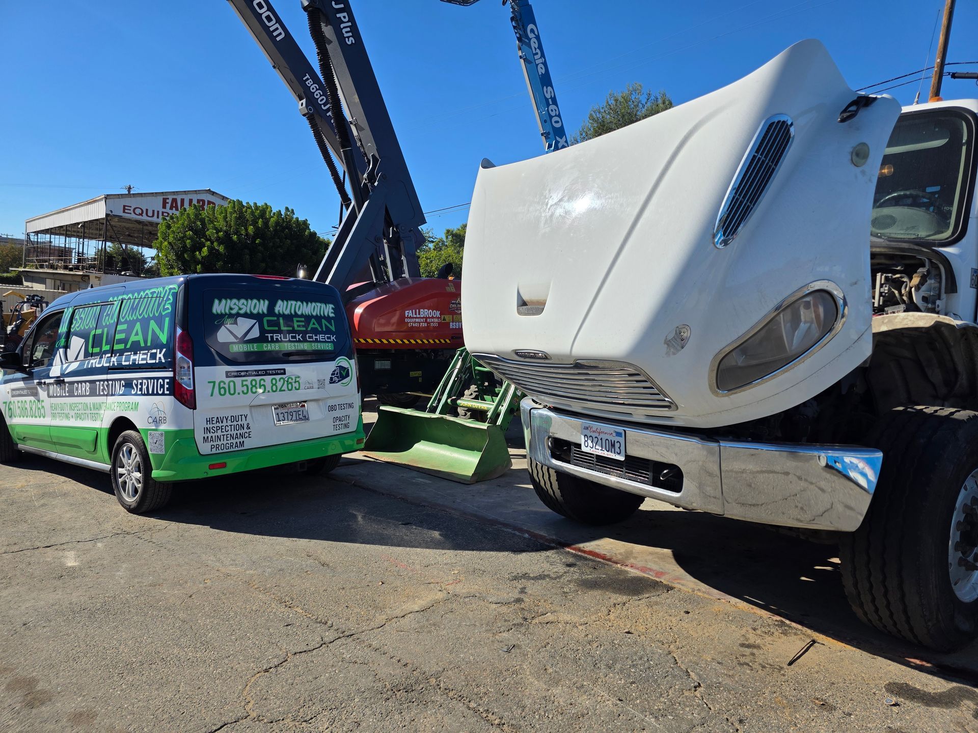 Tow truck lifting a green van with a white truck cab in a sunny lot, showing vehicle recovery work