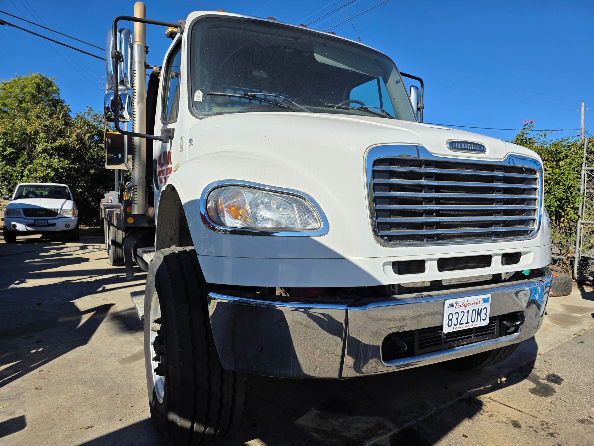 White utility truck parked on a sunny street, front view with chrome grille and clear blue sky.