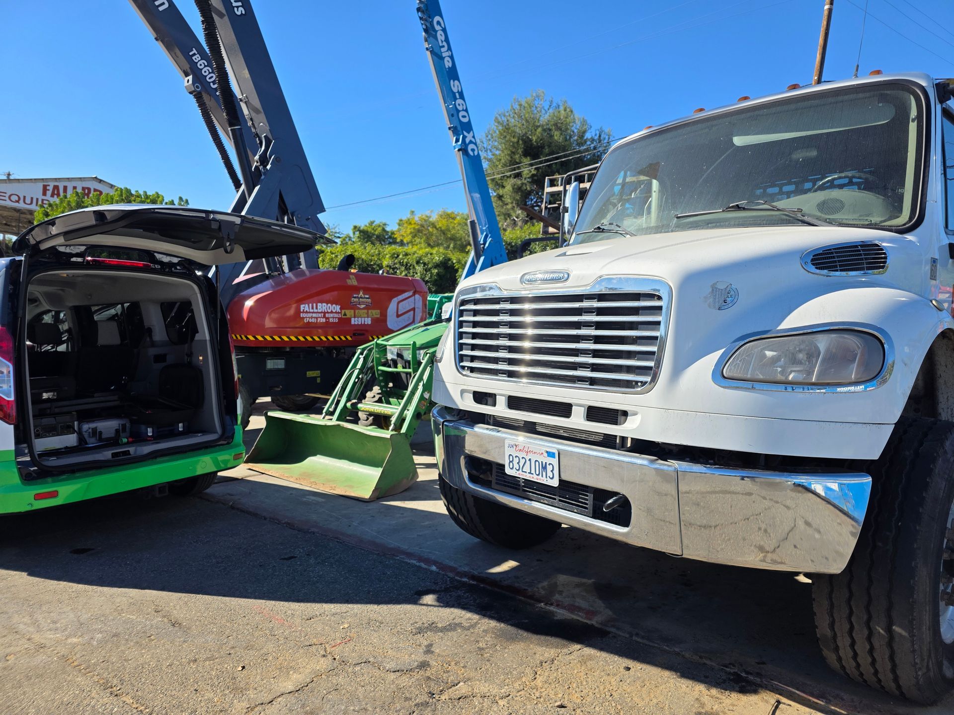 Tow truck lifting a green car beside a white truck at an outdoor lot