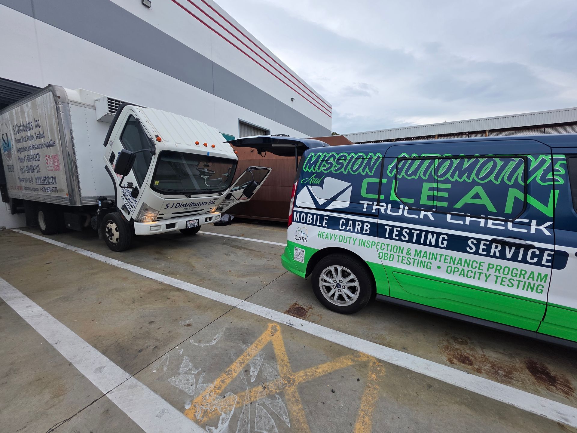Two trucks parked outside a building, one white and damaged, one green with service lettering.