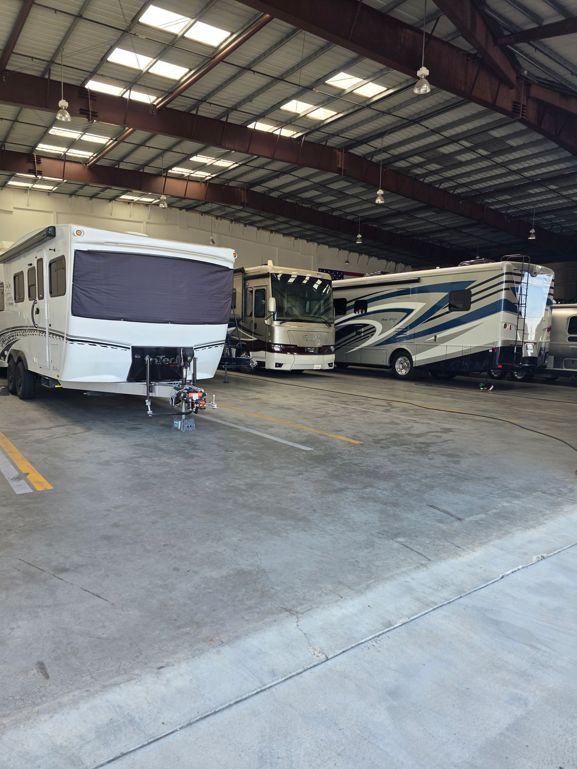 Three RVs parked inside a large warehouse with a concrete floor and metal roof.