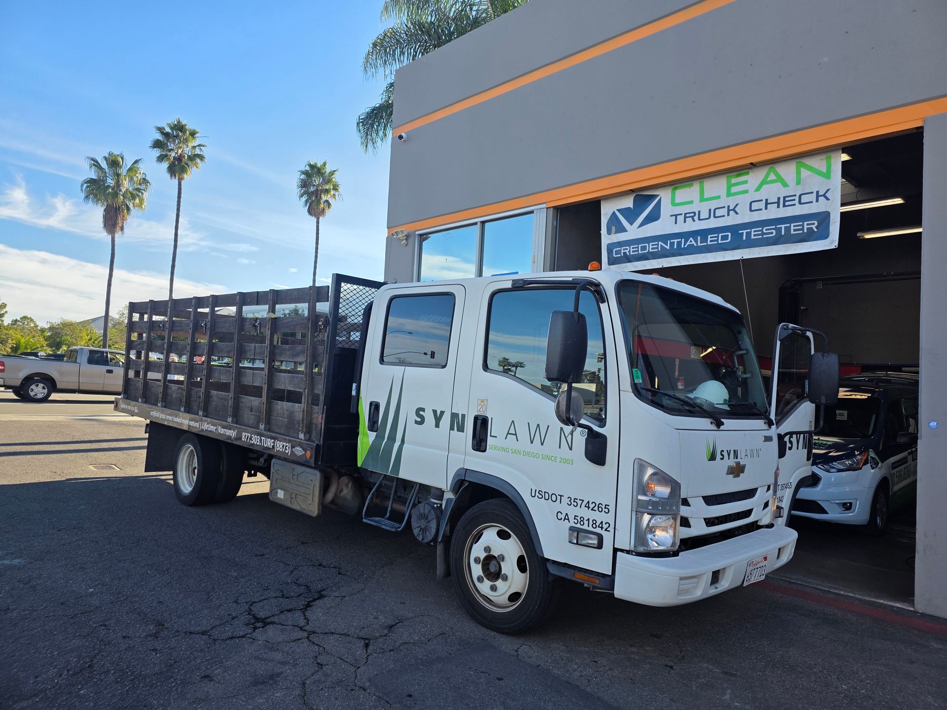 White dump truck parked outside a truck wash bay with “CLEAN” sign and another truck inside