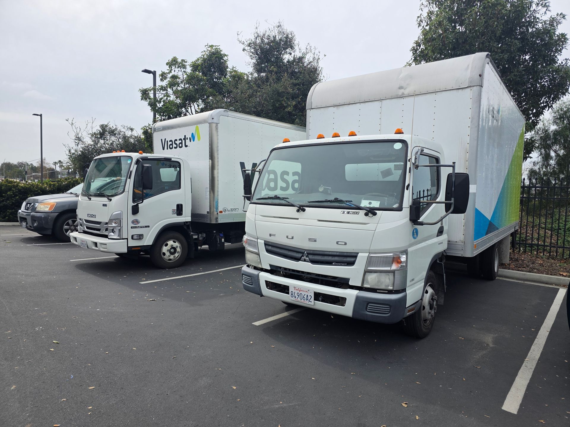 Two white box trucks parked in a lot, one with a cab-over body and another with green branding.