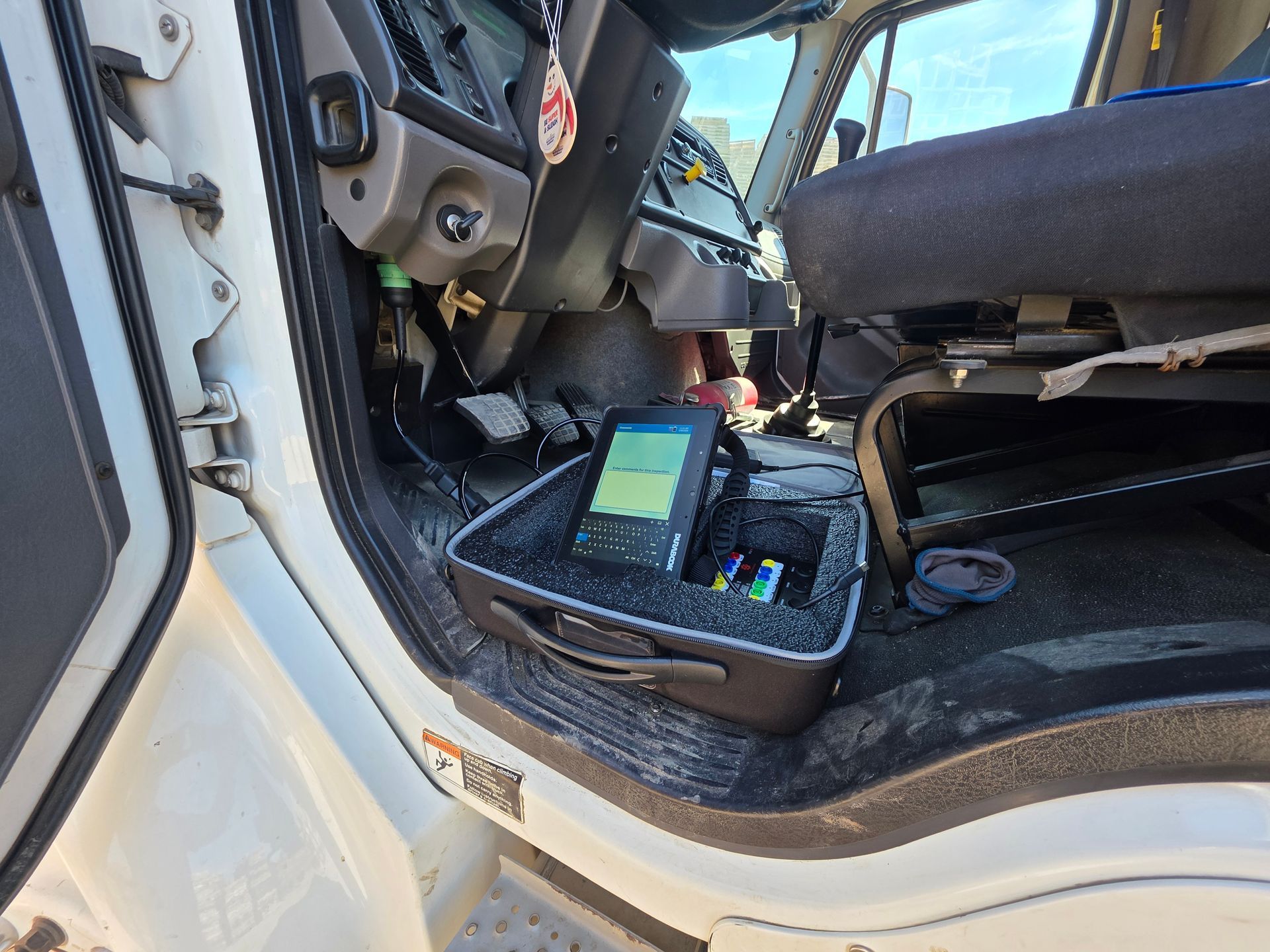 Car interior with a diagnostic tablet open on the passenger seat and the door open.