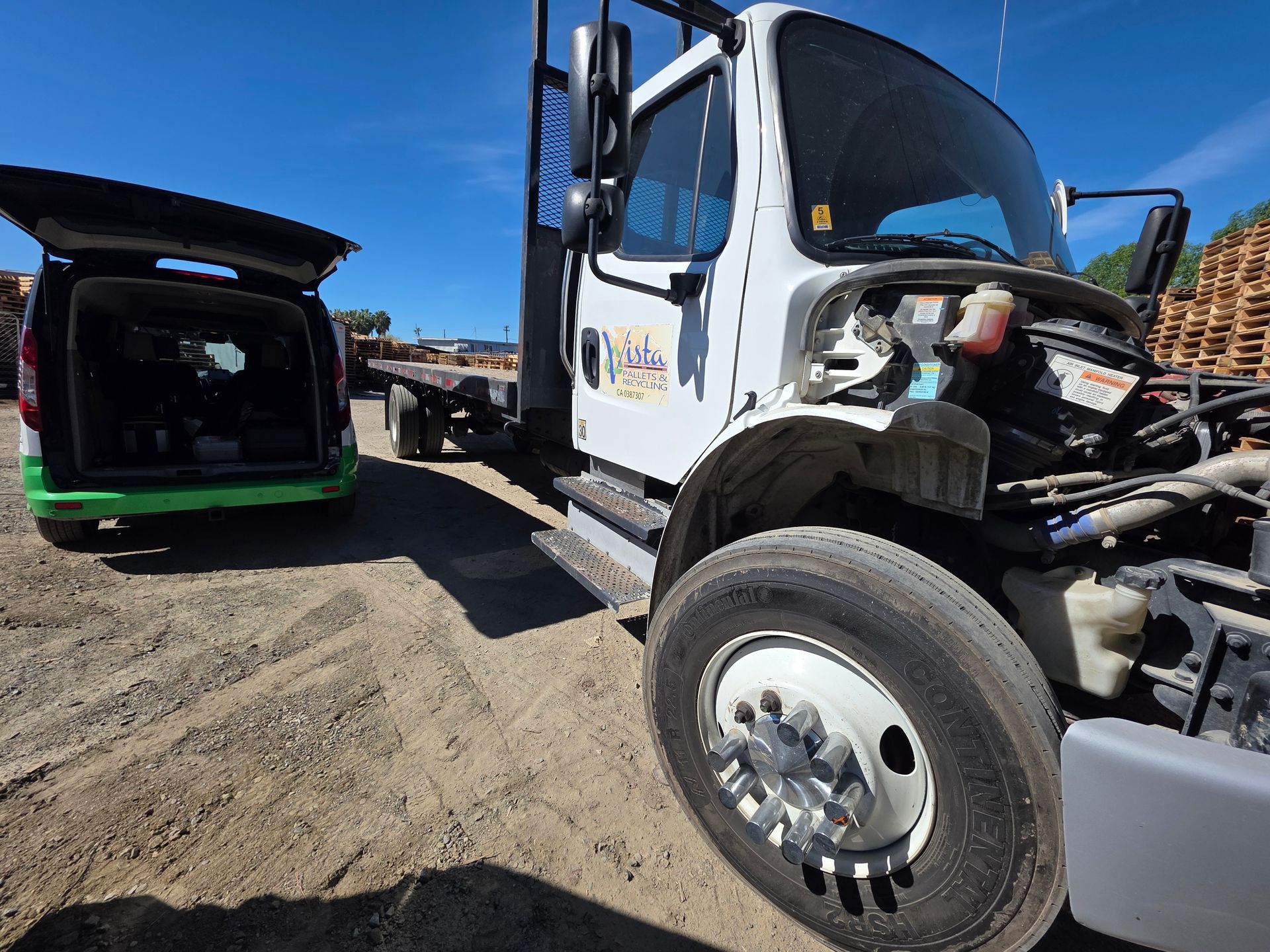 Tow truck lifting a green car in a sandy lot under a blue sky