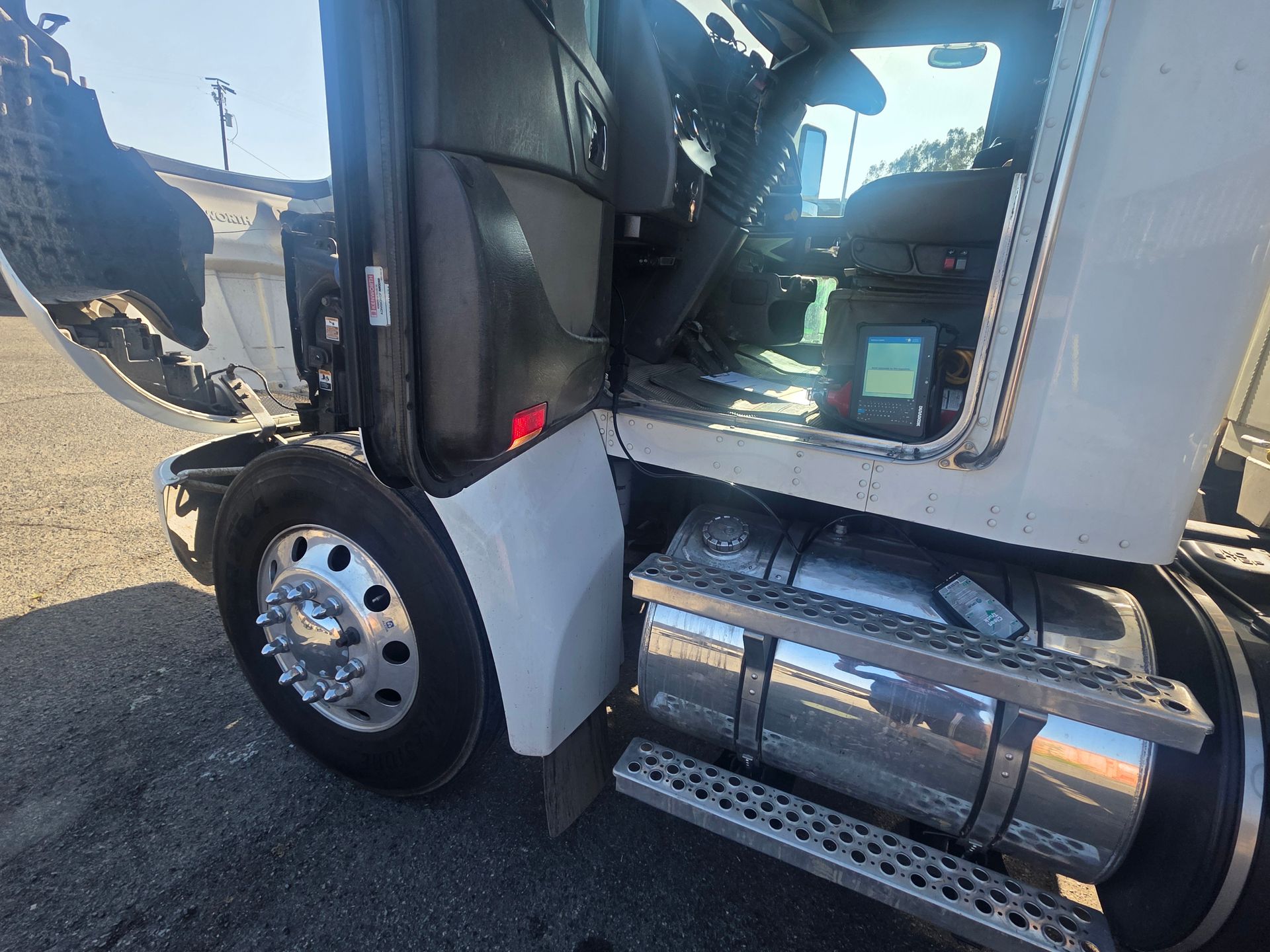 Close-up of a white semi-truck cab with open door, showing the front wheel and chrome fuel tank.