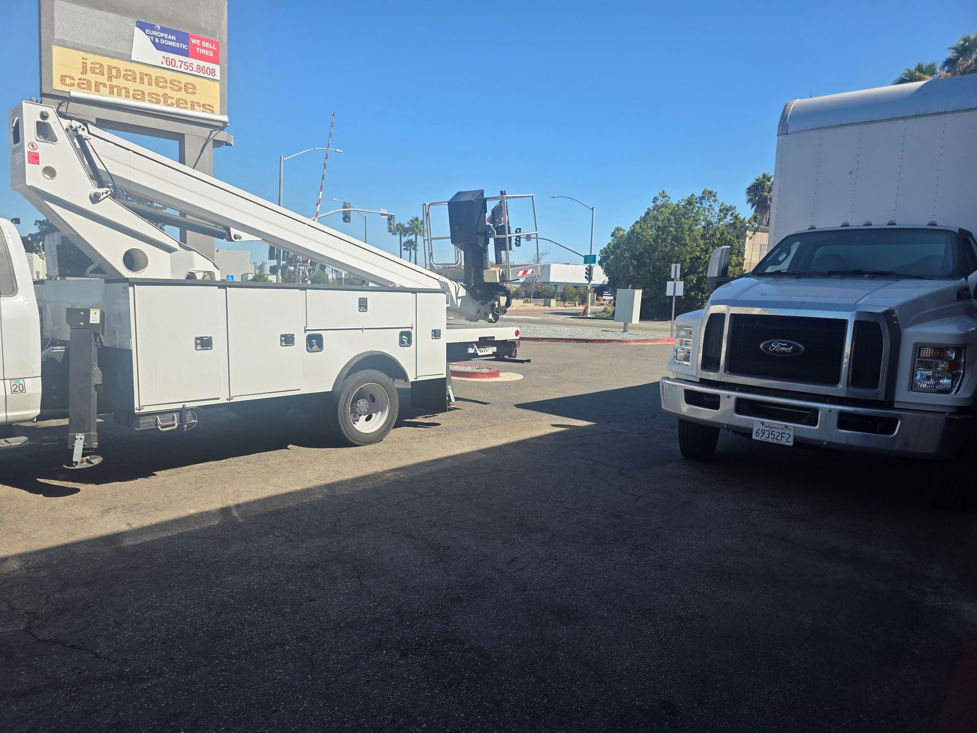 Utility trucks parked on a sunny street, including a white bucket truck and a white box truck